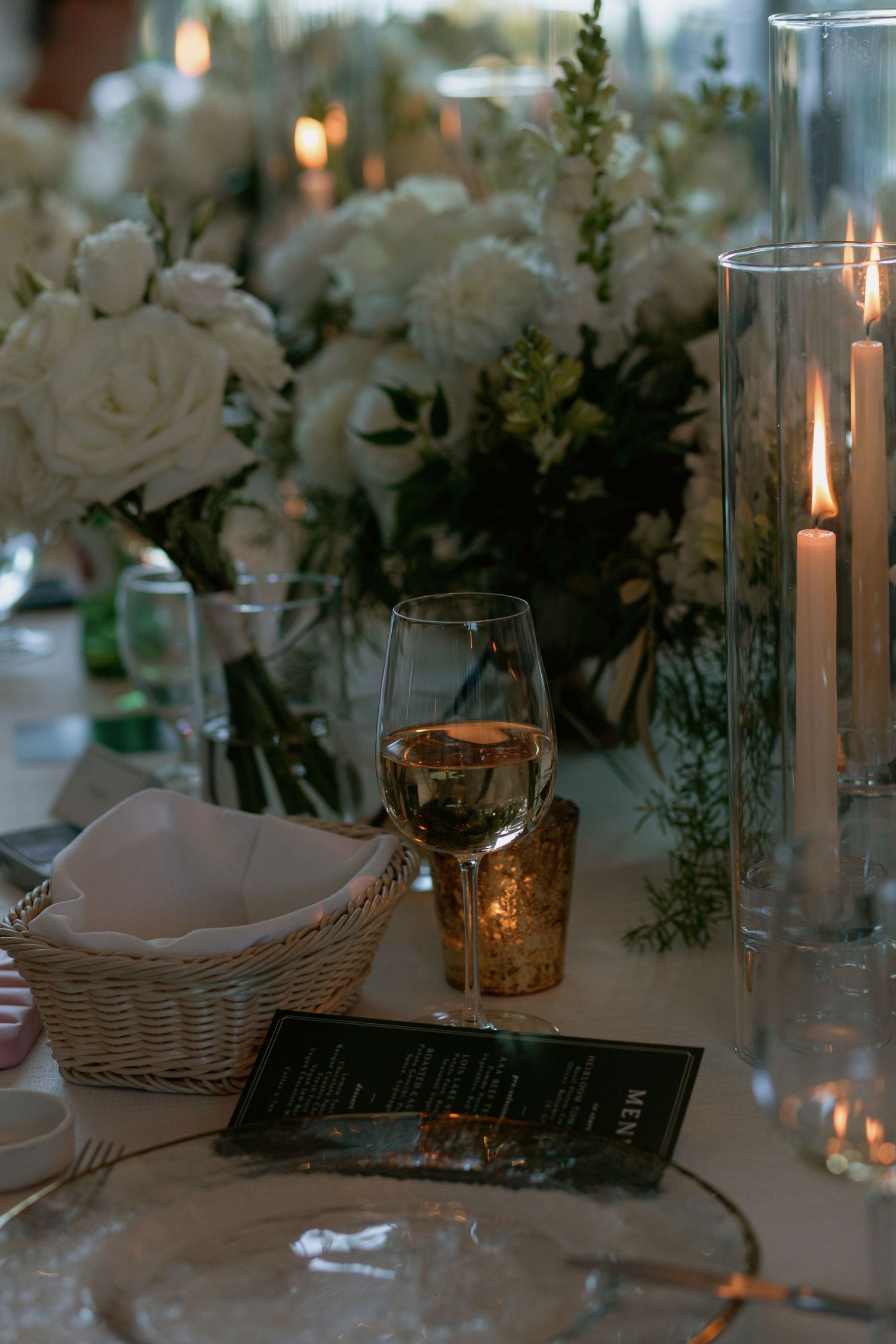 Wedding reception table decorated with white roses, candles in glass holders, and woven baskets.