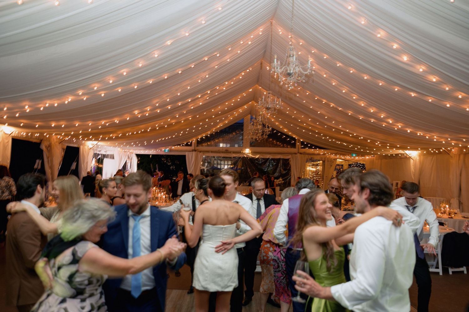 Guests enjoying themselves on the dance floor under a beautifully lit tent ceiling.