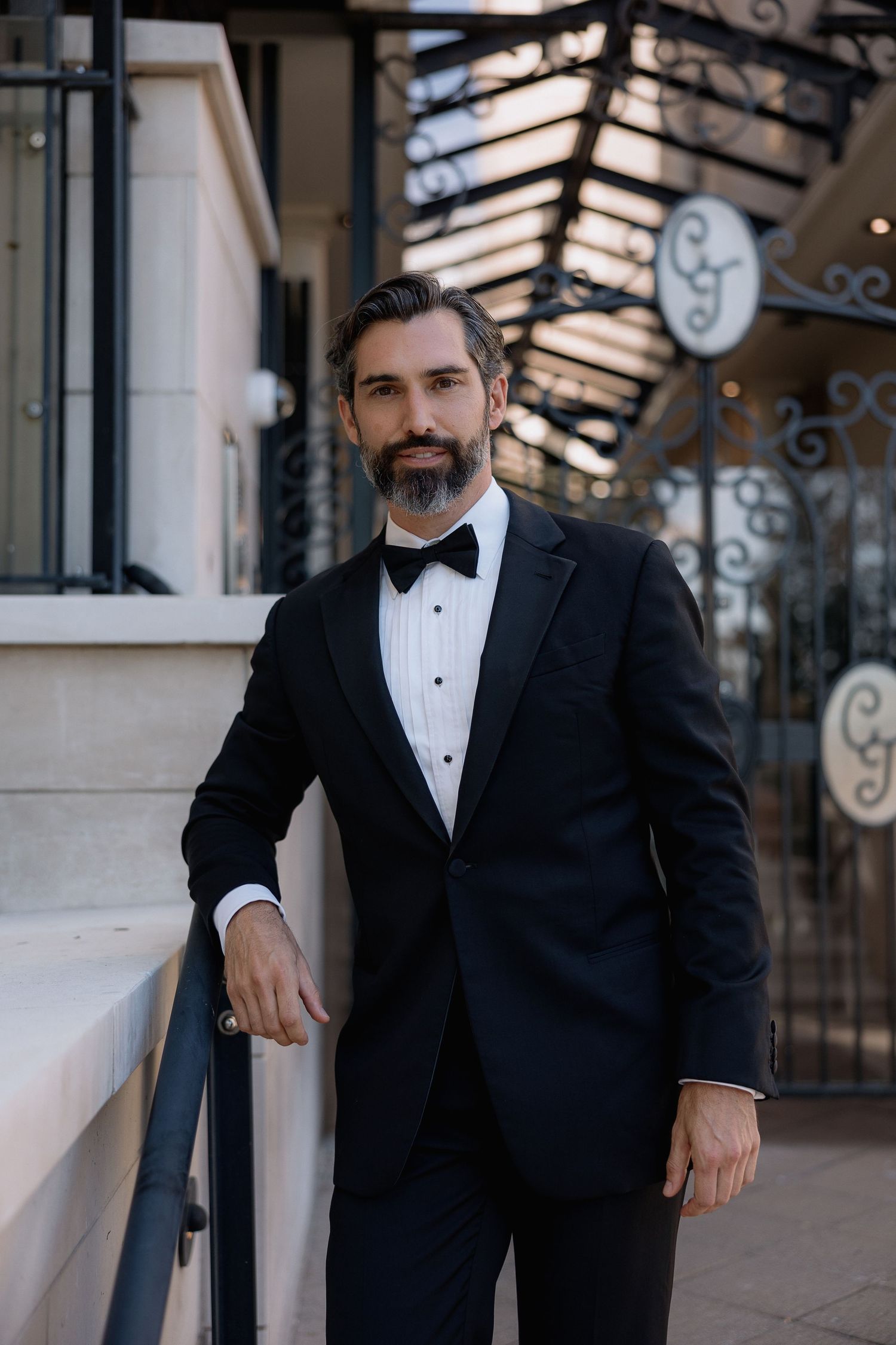 Groom in classic black tuxedo poses against architectural backdrop.