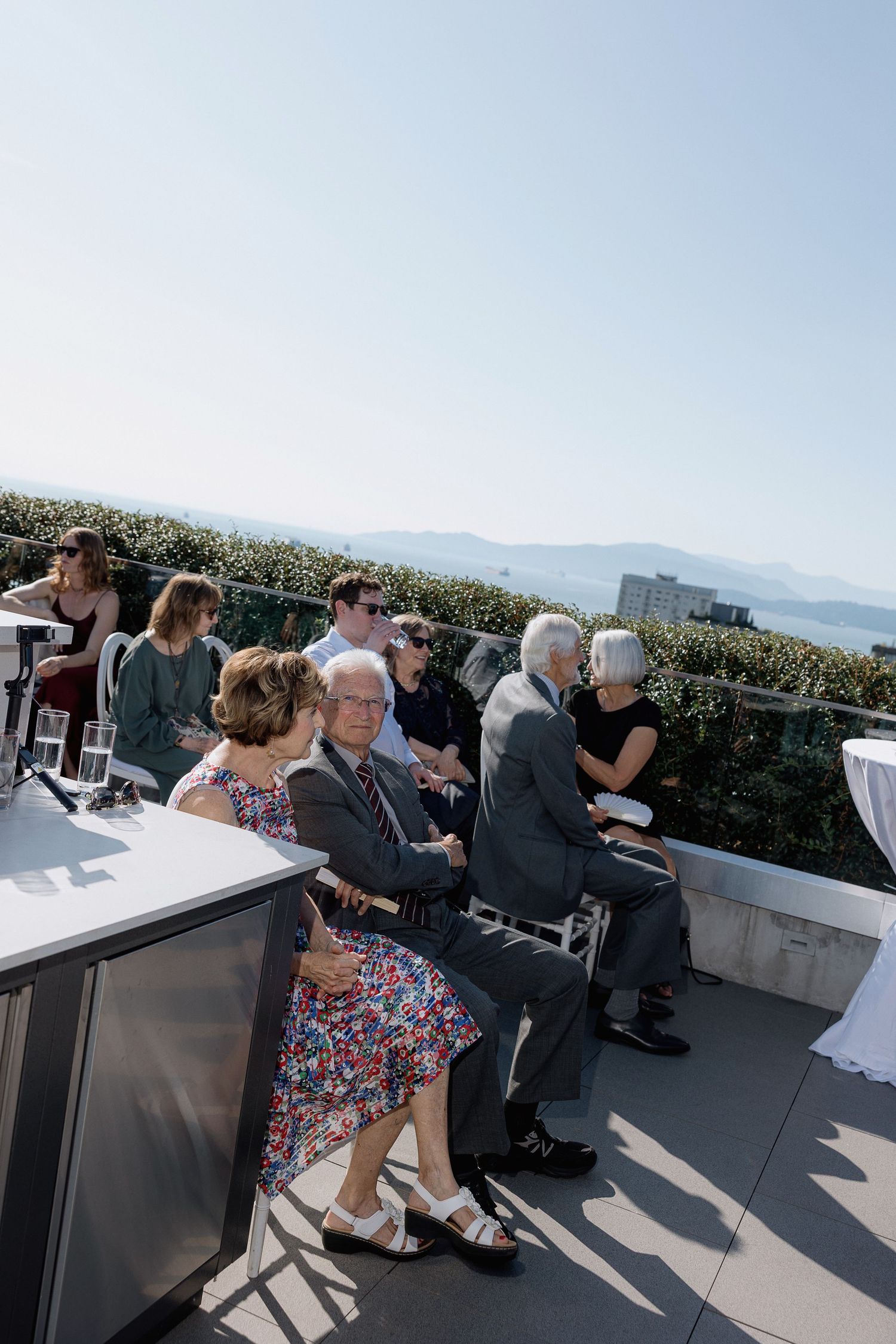 People seated on an outdoor patio overlooking mountain views on a sunny day.