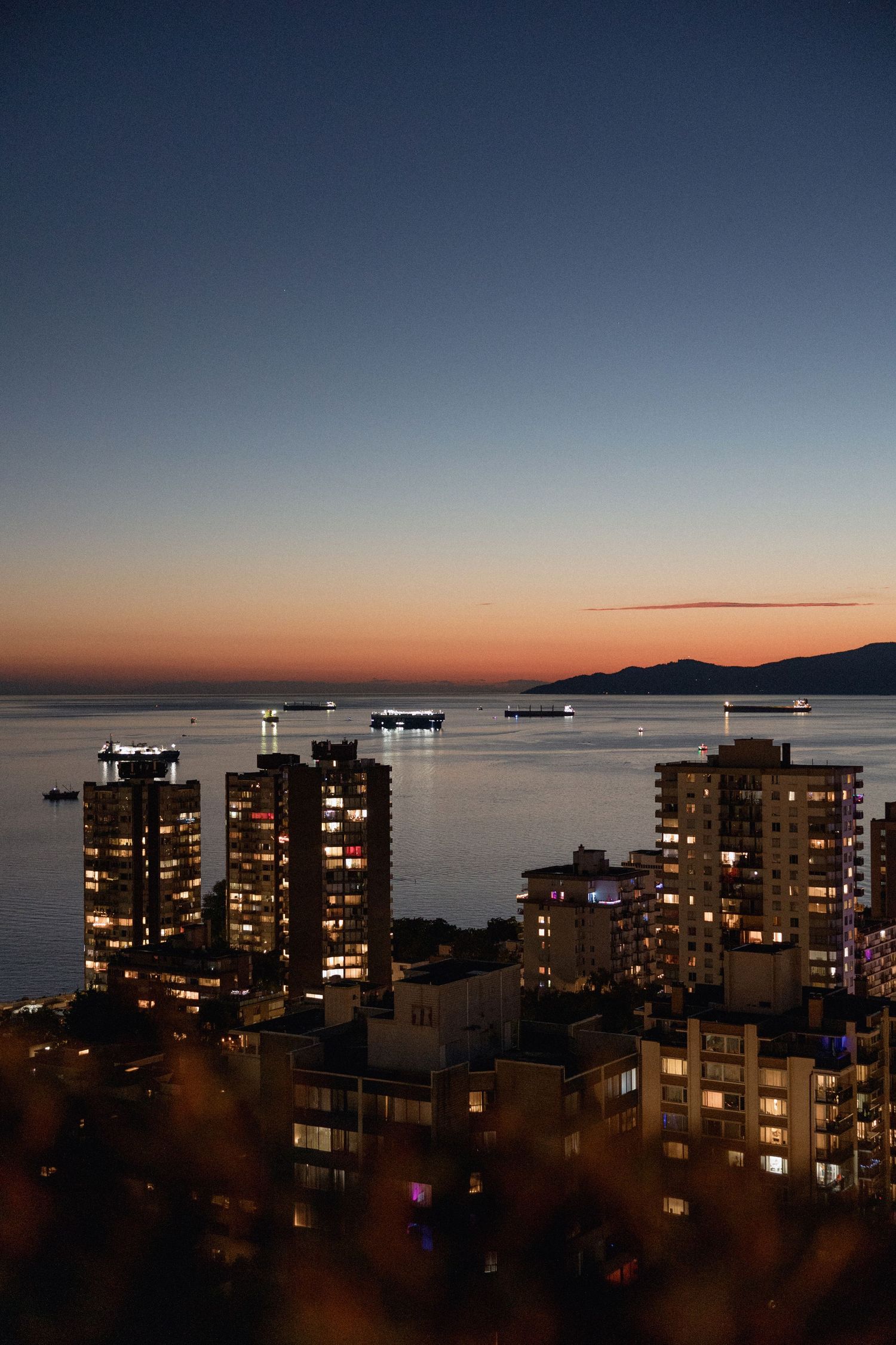 Cityscape at dusk showing illuminated apartment buildings along a waterfront English Bay in Vancouver