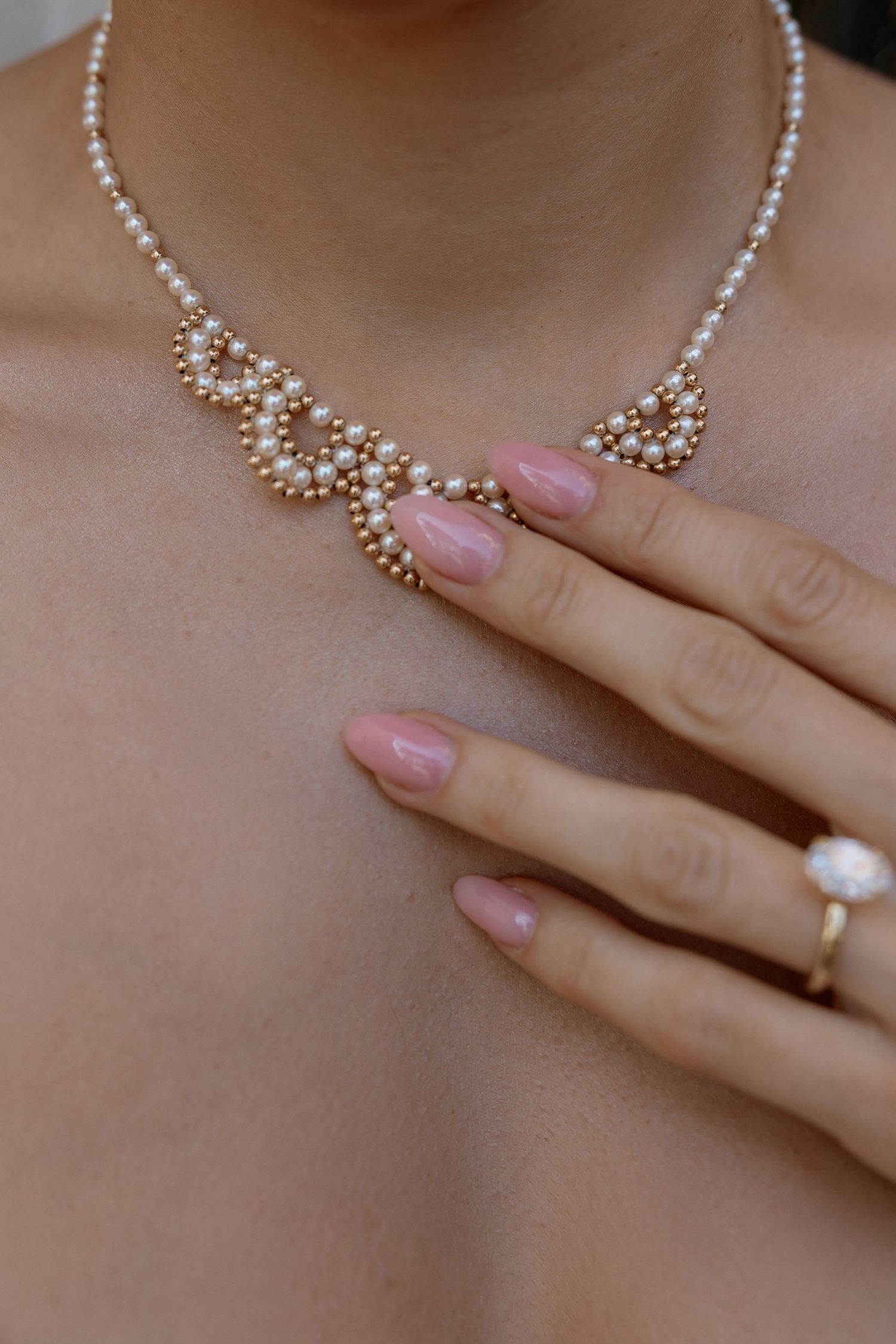Delicate pearl necklace and ring with pink manicured nails close-up.