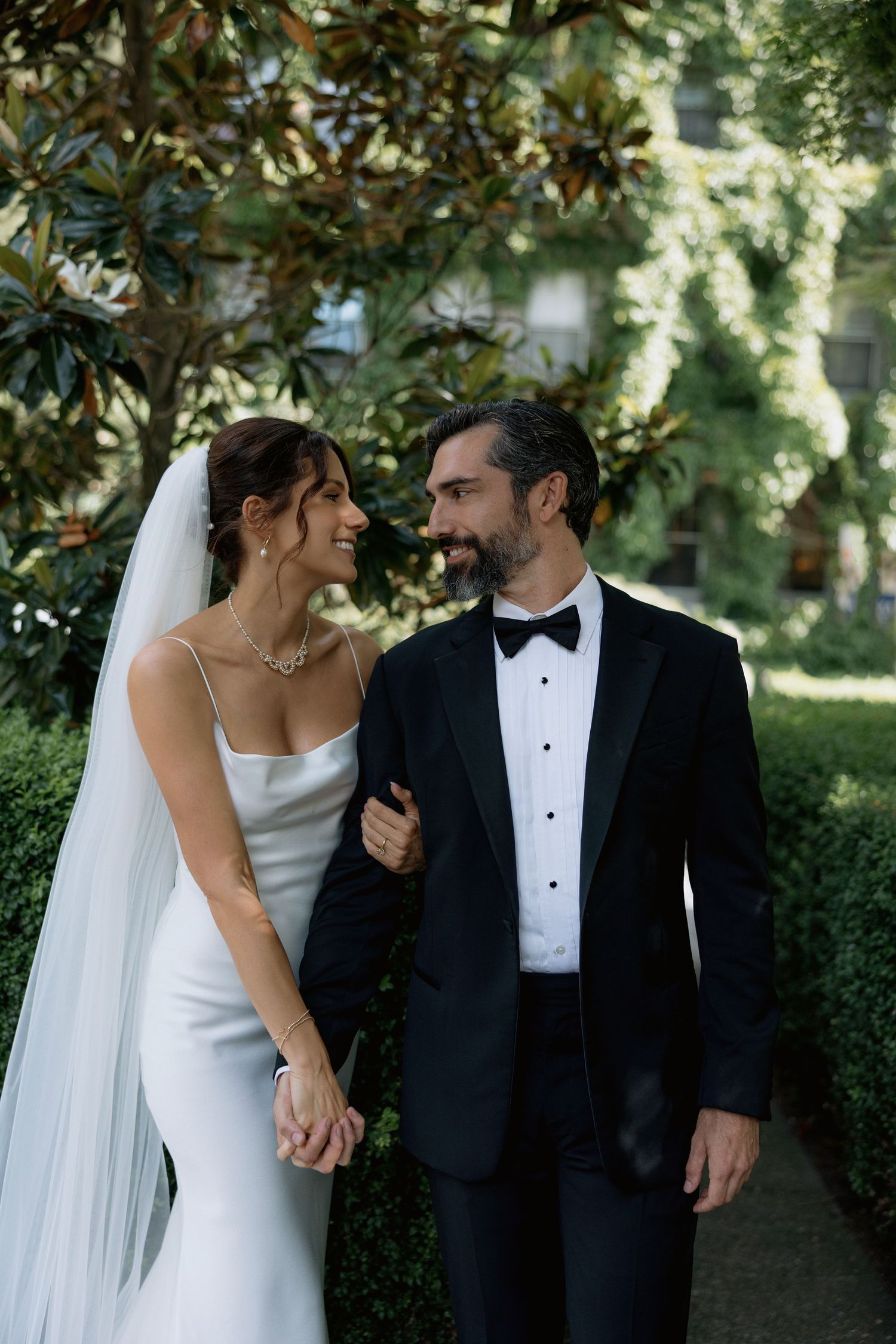 Newlywed couple shares romantic moments in garden setting with magnolia trees and natural light in front of the Sylvia Hotel in Vancouver