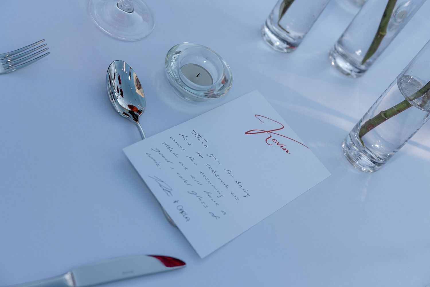 Place settings and wine glasses arranged on white tablecloths at formal event.
