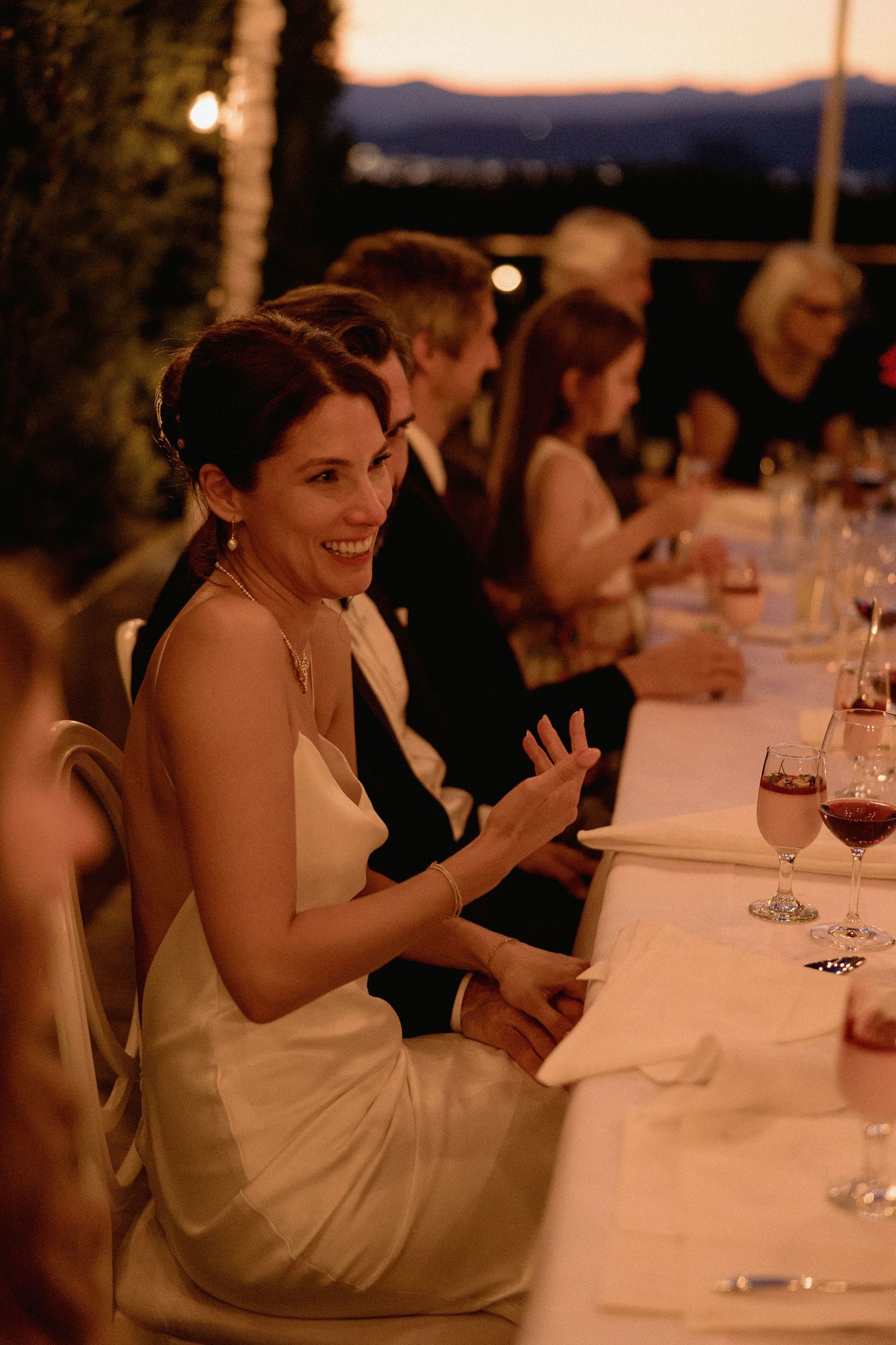 Elegant outdoor wedding reception dinner with guests seated at a long table at sunset.