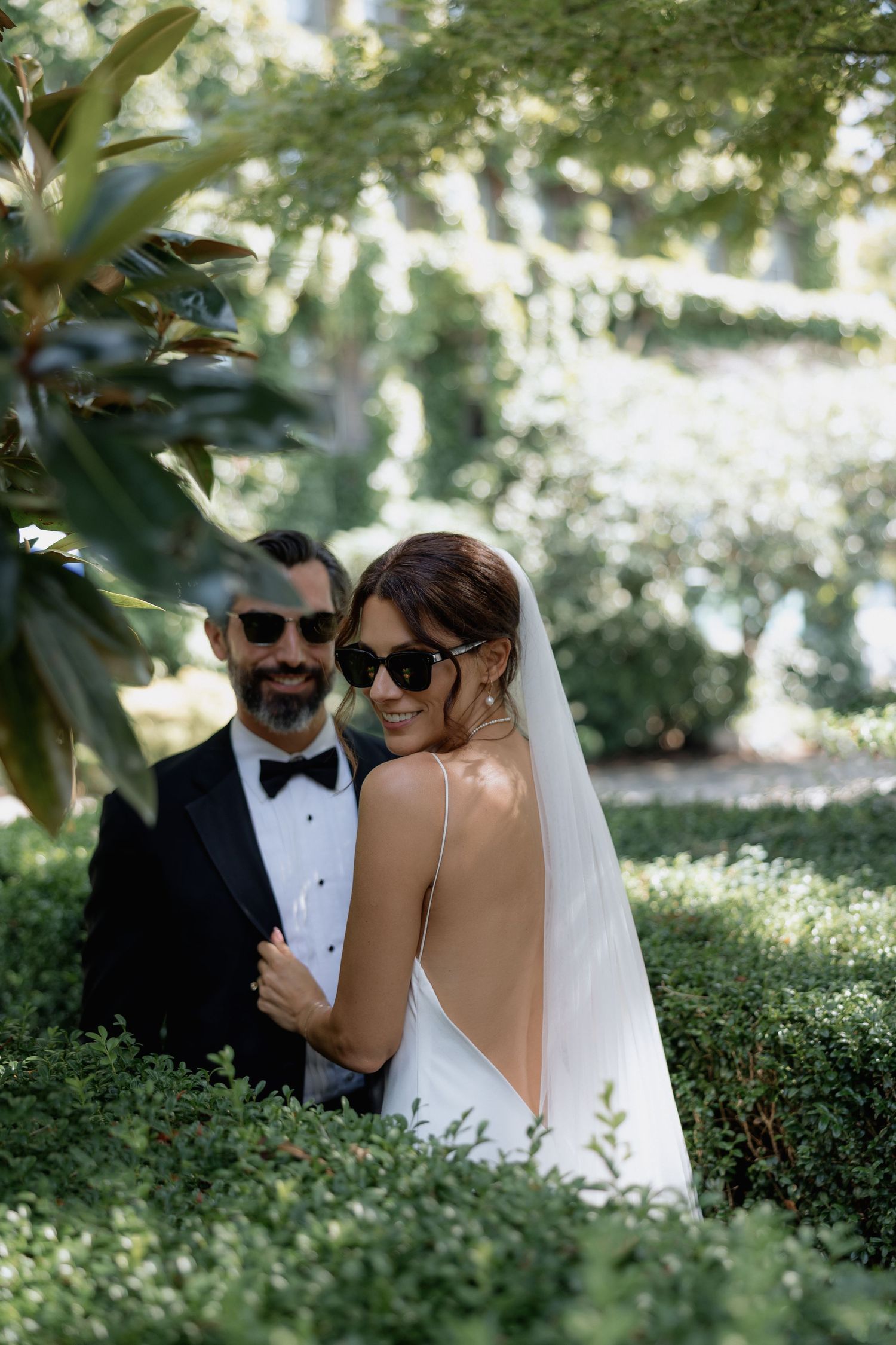 A couple in formal wedding attire poses among manicured garden hedges on their special day.