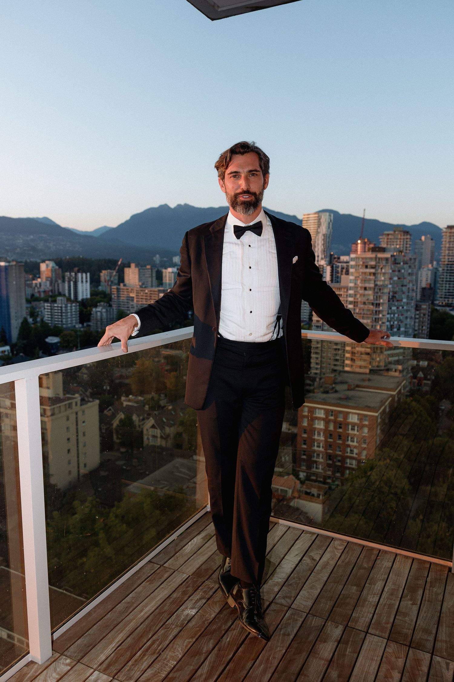Evening cityscape view from rooftop balcony with formal attire and mountain backdrop.