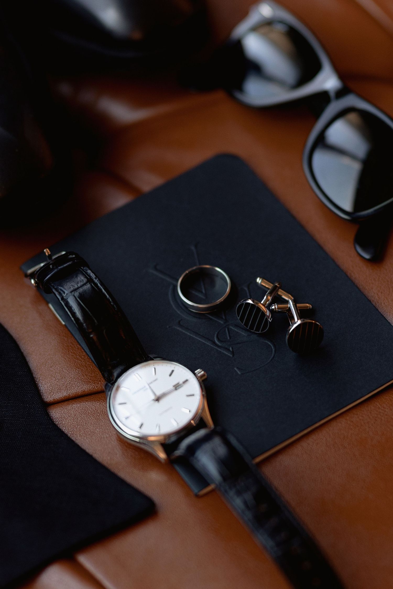 Elegant watch and accessories displayed on a black surface with warm lighting.