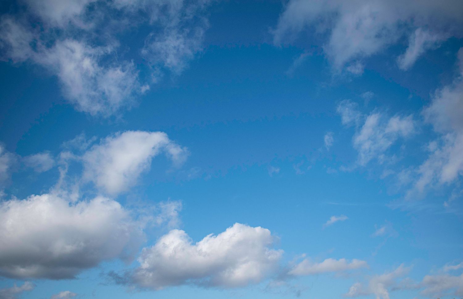 Bright blue sky with fluffy white cumulus clouds scattered across, perfect for backgrounds or weather-related content.