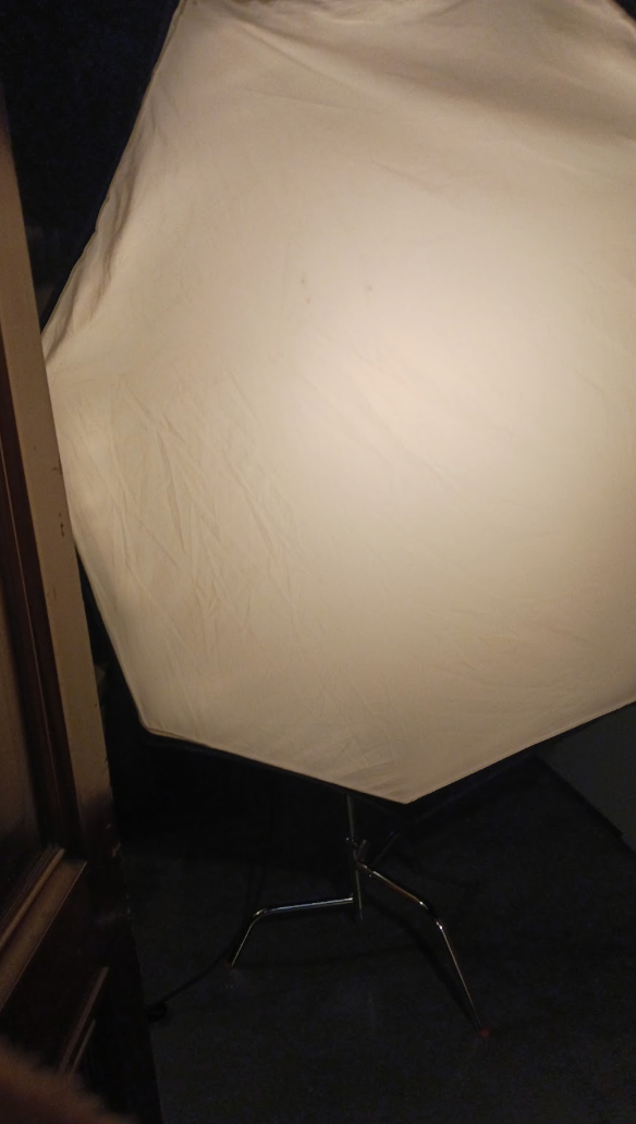 Large octagonal photography softbox diffuser on a light stand against a dark background.