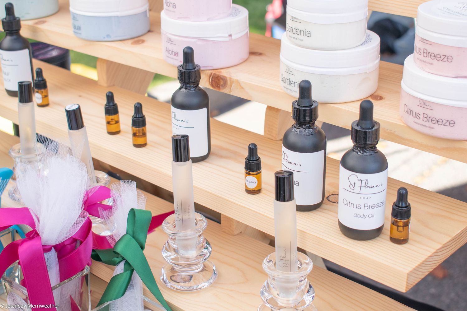 Wooden shelf display of essential oil dropper bottles and skincare products at an outdoor market.