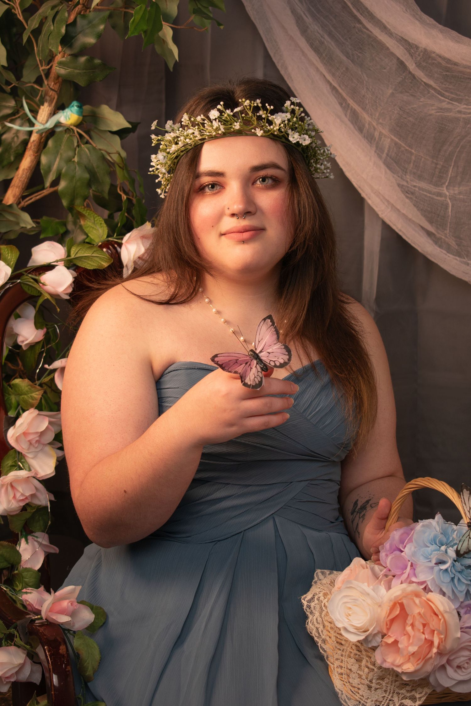 Young woman in blue dress holding butterfly with floral crown and basket of flowers.