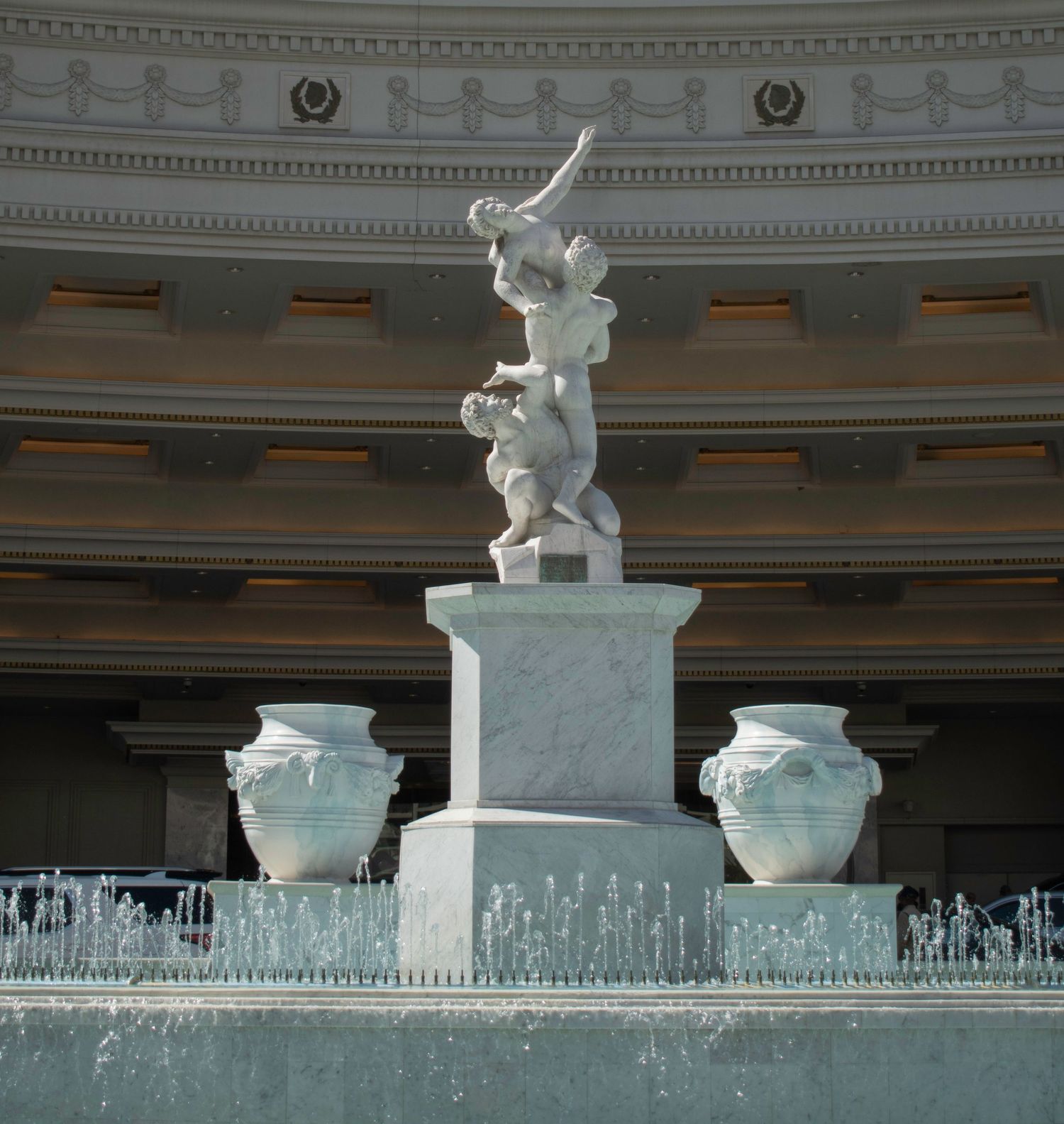 Elegant white marble fountain statue of cherubs on a pedestal at a grand classical building.