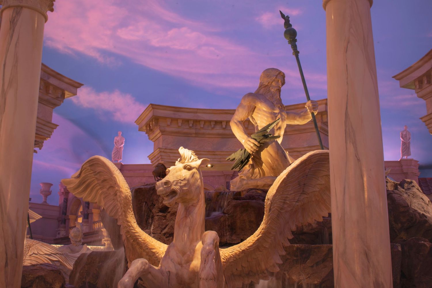 Golden statue of Neptune with spear riding winged horses inside ornate Roman-themed interior.