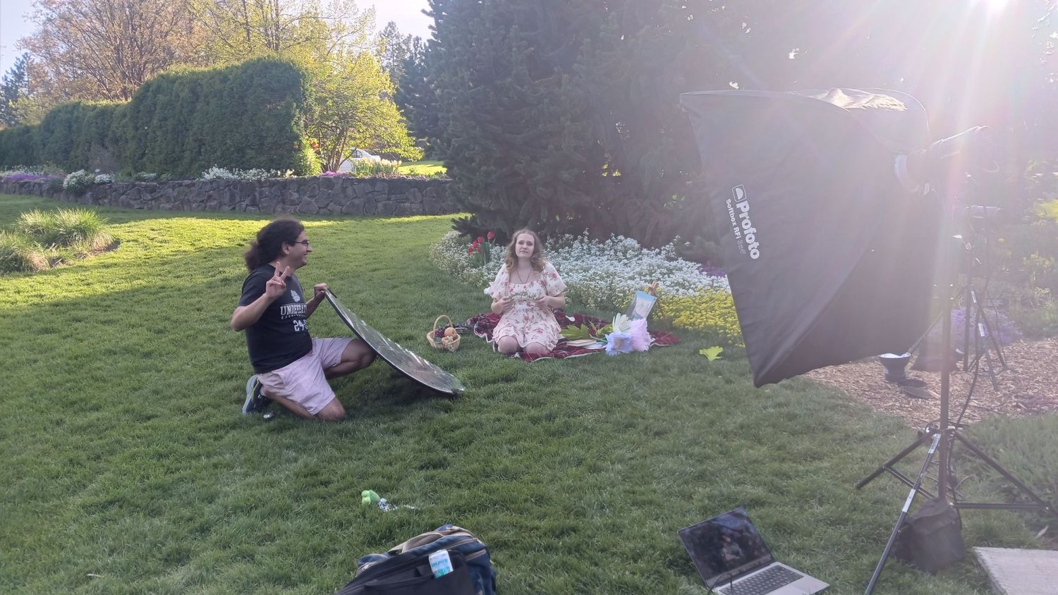 Outdoor photography session with photographer using reflector to capture young girl sitting on grass in garden.