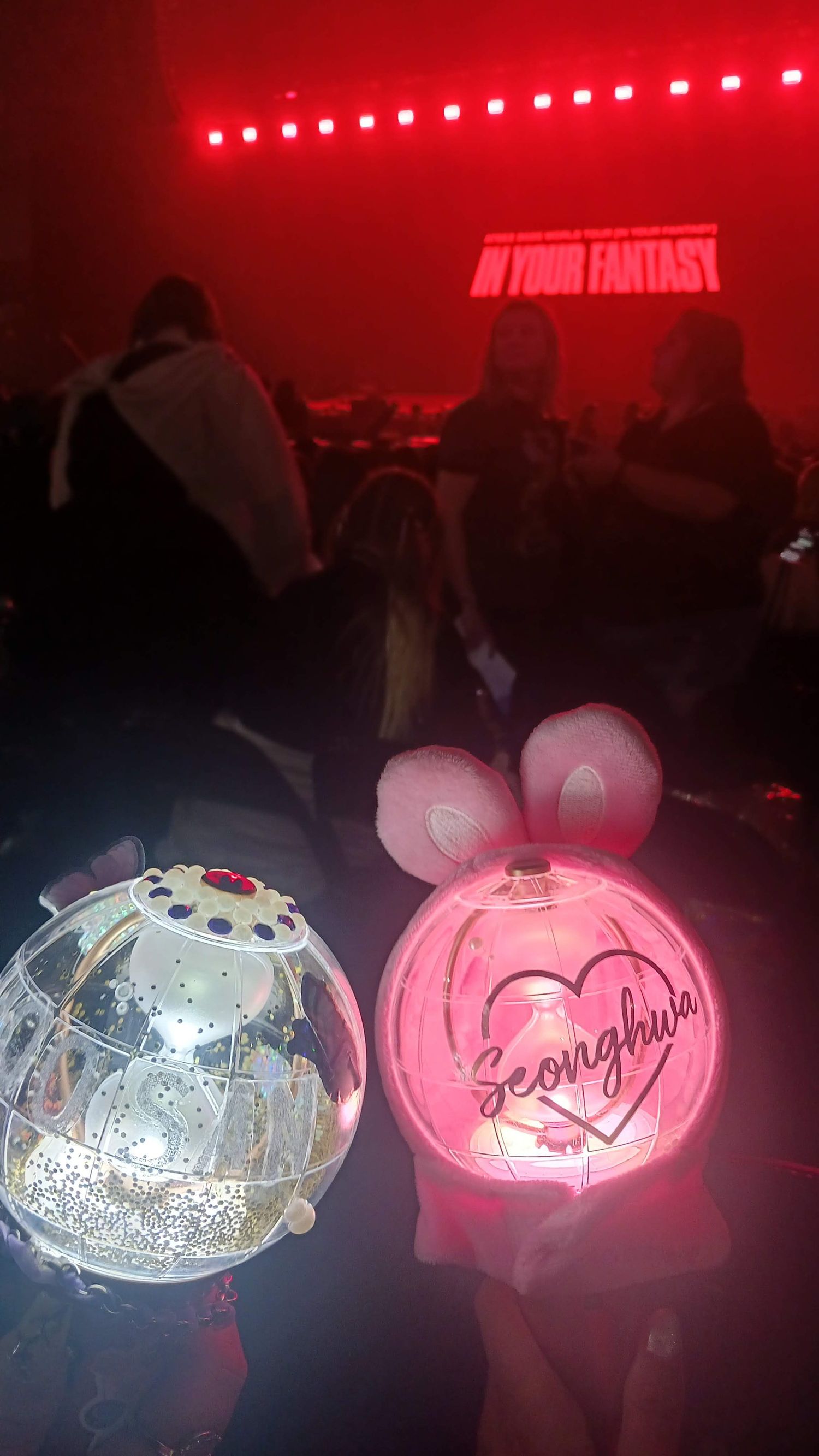 Two glowing fan light sticks at a K-pop concert with red lights and 