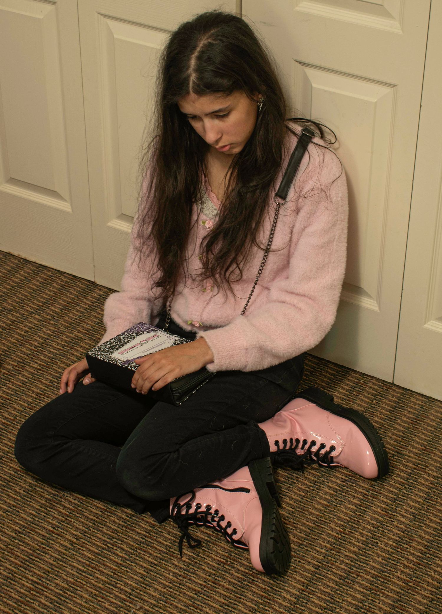 Young woman with long dark hair sits cross-legged on floor wearing pink fuzzy sweater and pink lace-up boots.