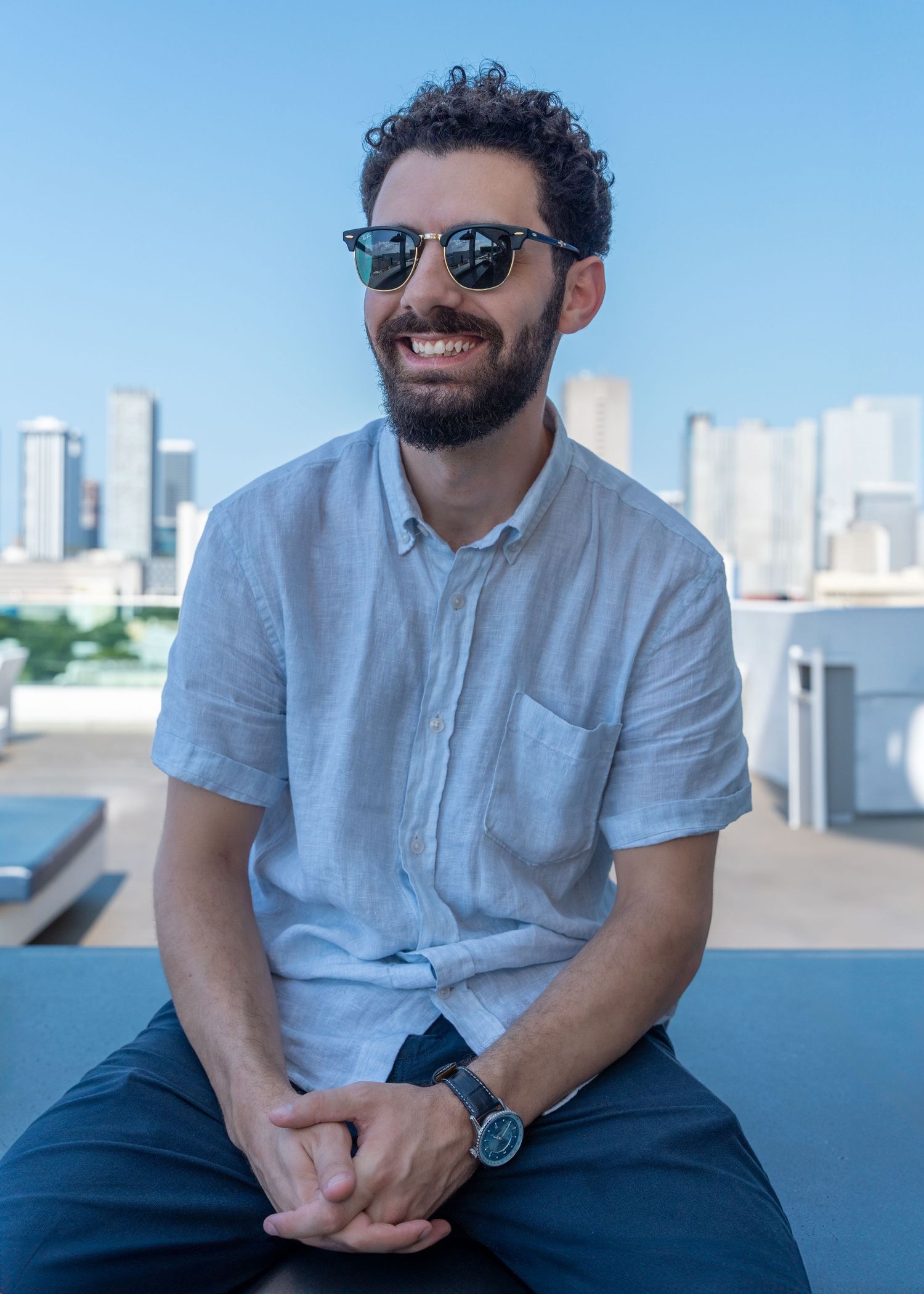 Lifestyle branding portrait of an entrepreneur seated outdoors with a city skyline in the background, captured with a relaxed, editorial fee