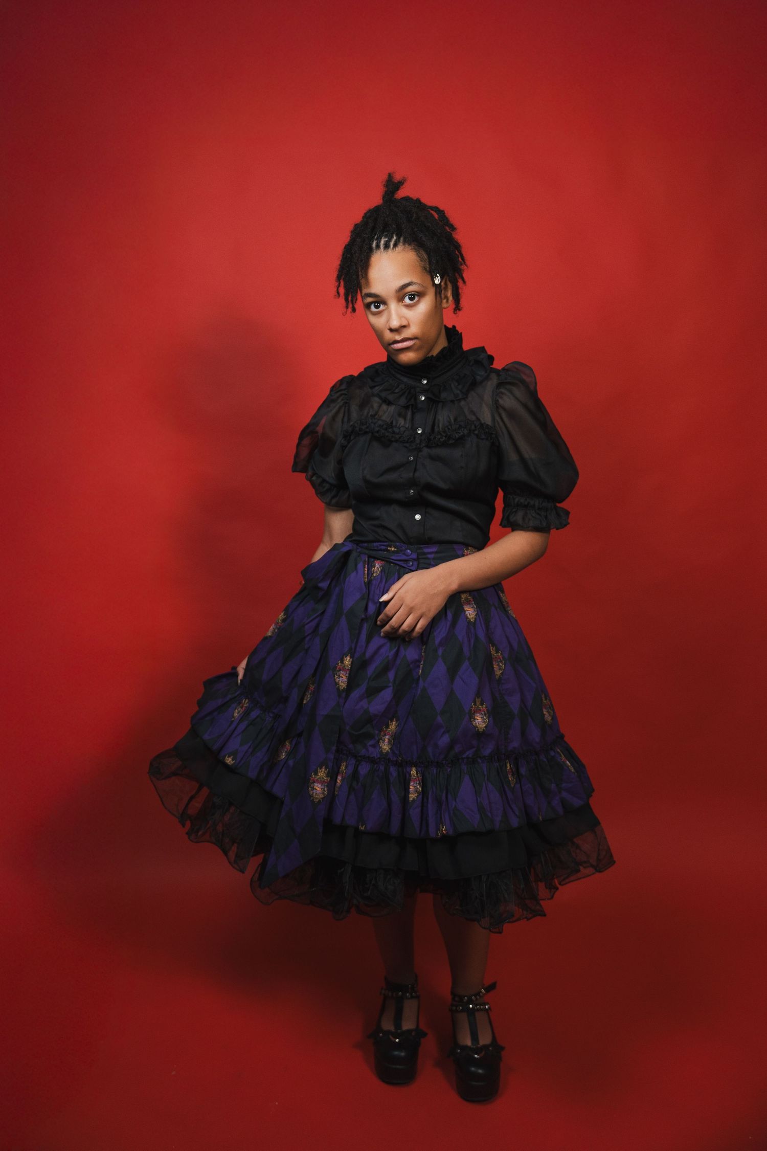 Studio birthday portrait featuring a graduate in a layered dress, posed confidently against a striking red backdrop.
