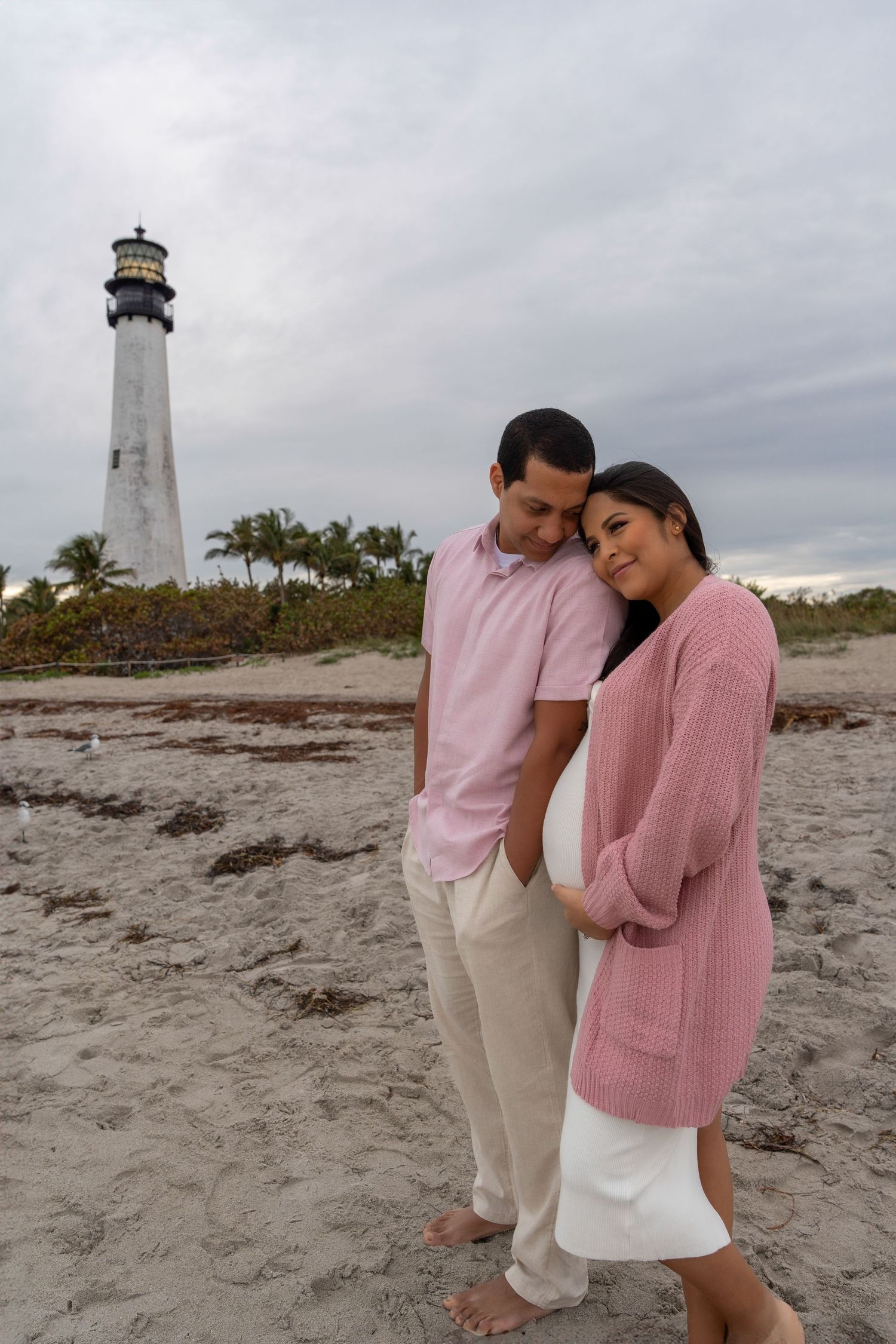 Couple walking along the beach near Hillsboro Inlet Lighthouse in Pompano Beach during a coastal maternity shoot.