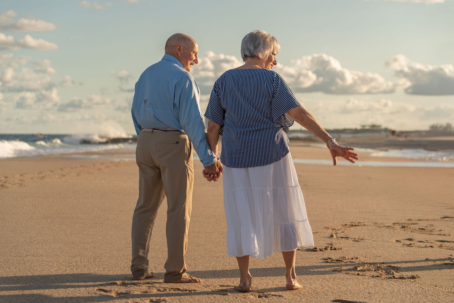 Senior couple walking hand-in-hand in Boynton Beach, FL – enjoying a peaceful golden hour beach moment.