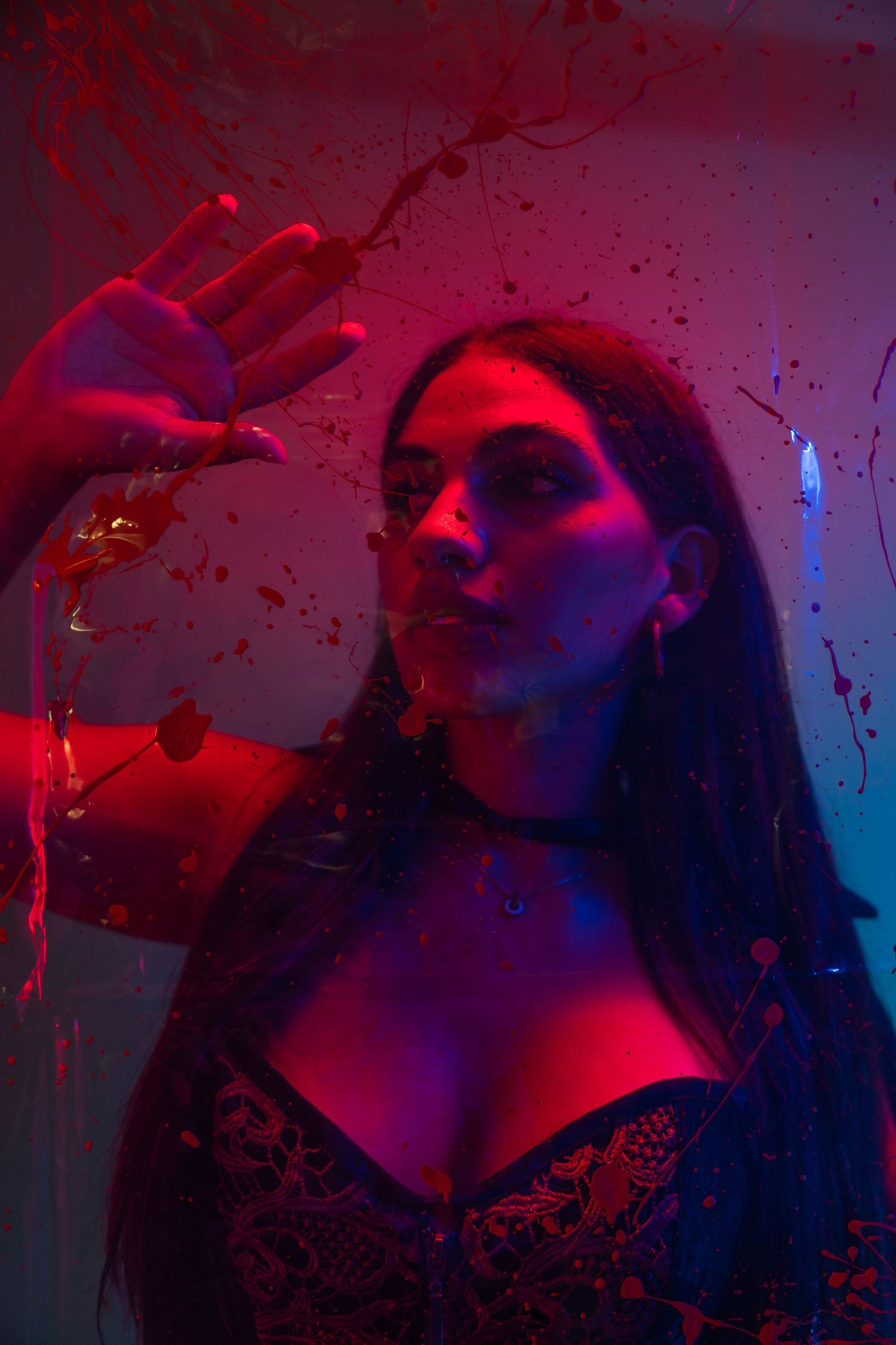 Dark fantasy portrait in Miami, FL – woman behind glass with dramatic neon lighting and blood effect.