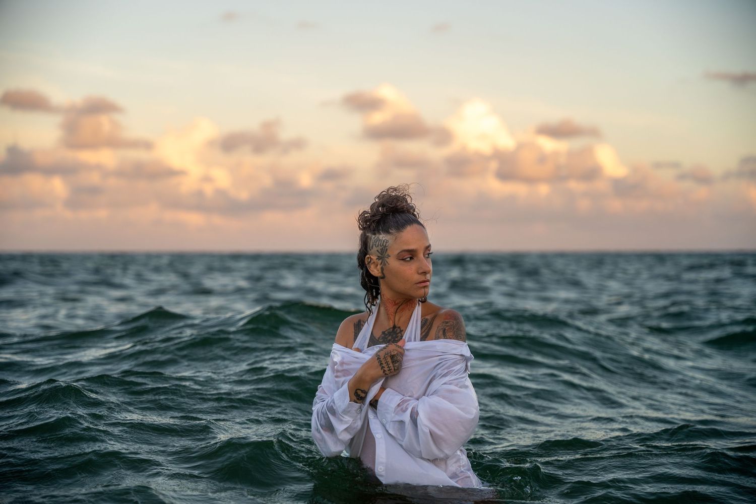 Ethereal ocean portrait of a woman standing waist-deep in the water, wrapped in a flowing white blouse as the pastel sky meets the horizon.