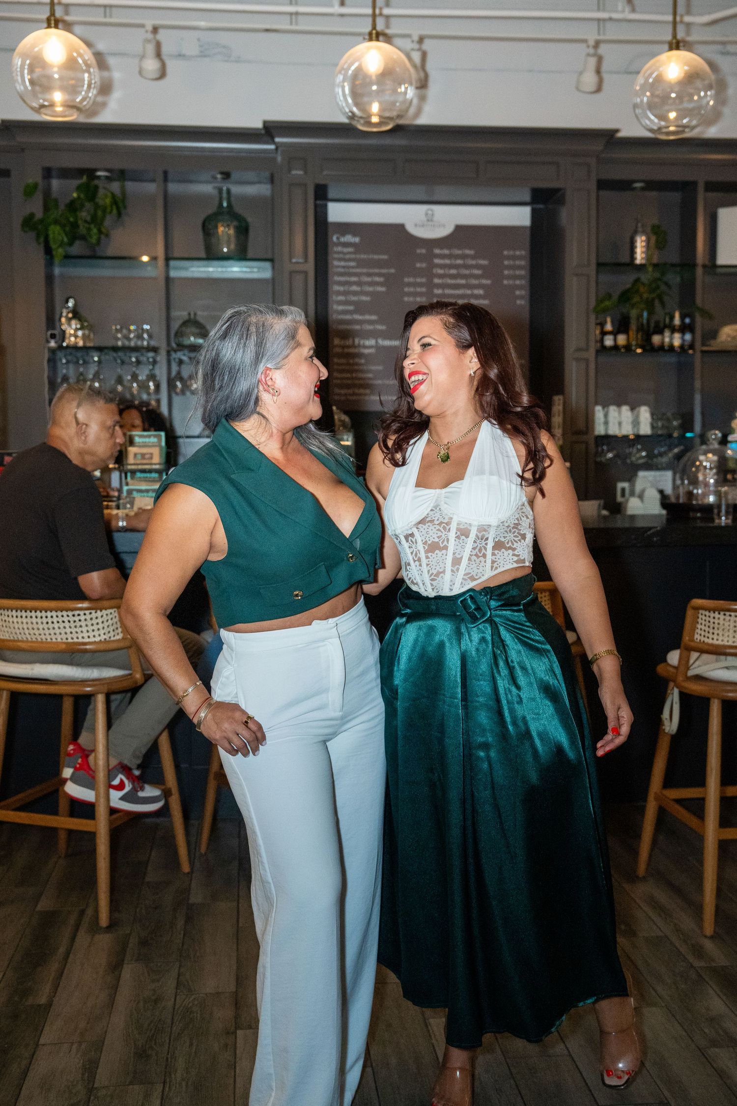 Two women celebrating together inside Bartolo Café during a grand opening event in Delray Beach.