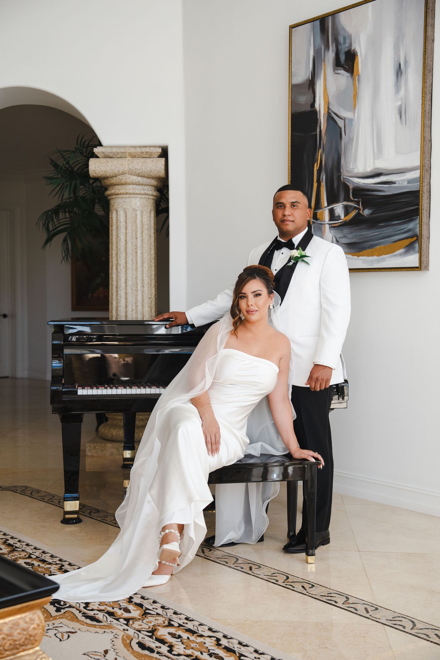 Elegant indoor wedding portrait of a bride and groom posing beside a grand piano, captured with a refined documentary-editorial style.