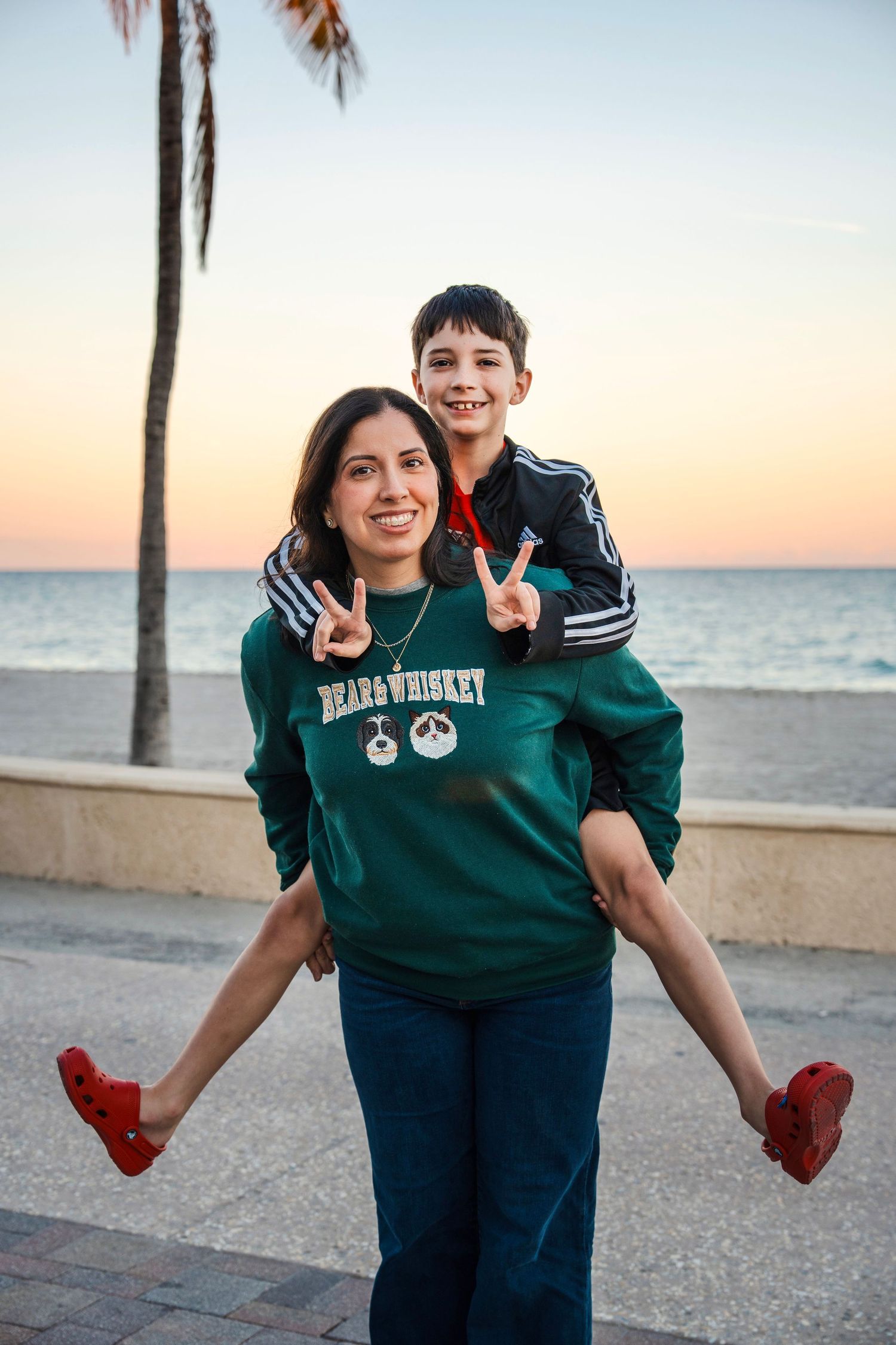 Playful beach family portrait of a mother giving her child a piggyback ride at sunset in South Florida.