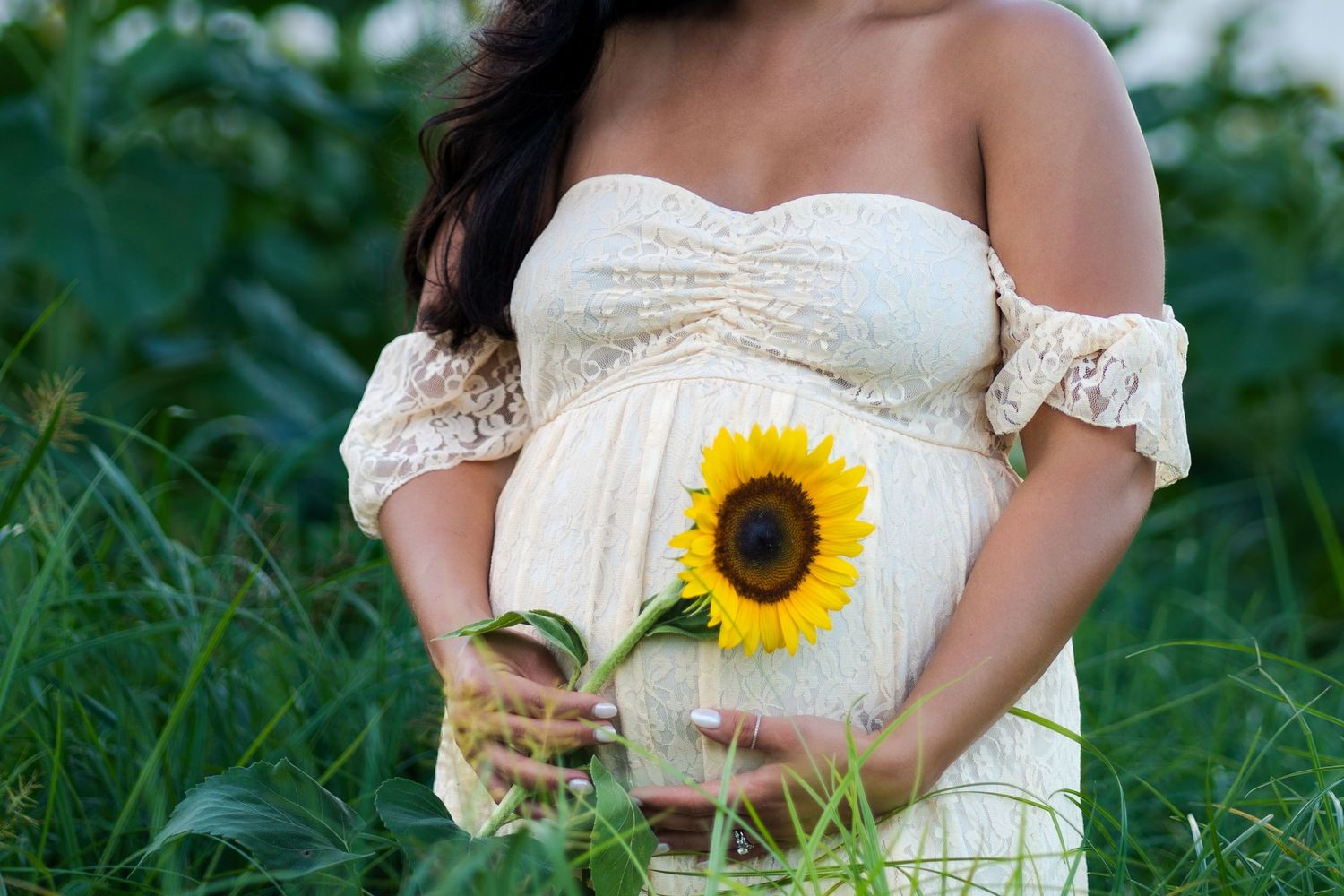 Close-up maternity portrait with sunflower bouquet, soft lace dress, and greenery in Homestead, Florida.