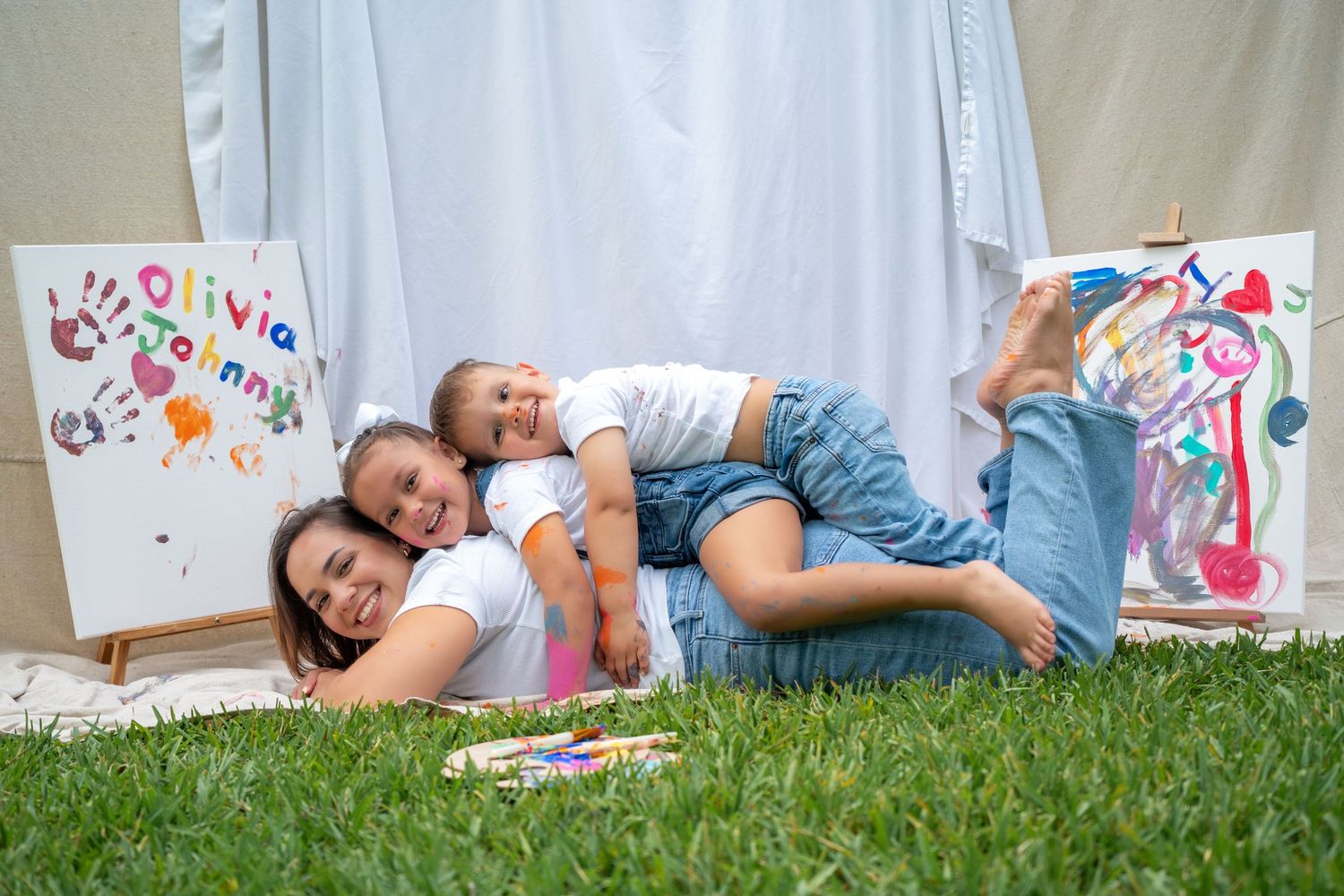 Mother and two kids laughing while laying on the grass during a Mommy & Me painting session in Miami.