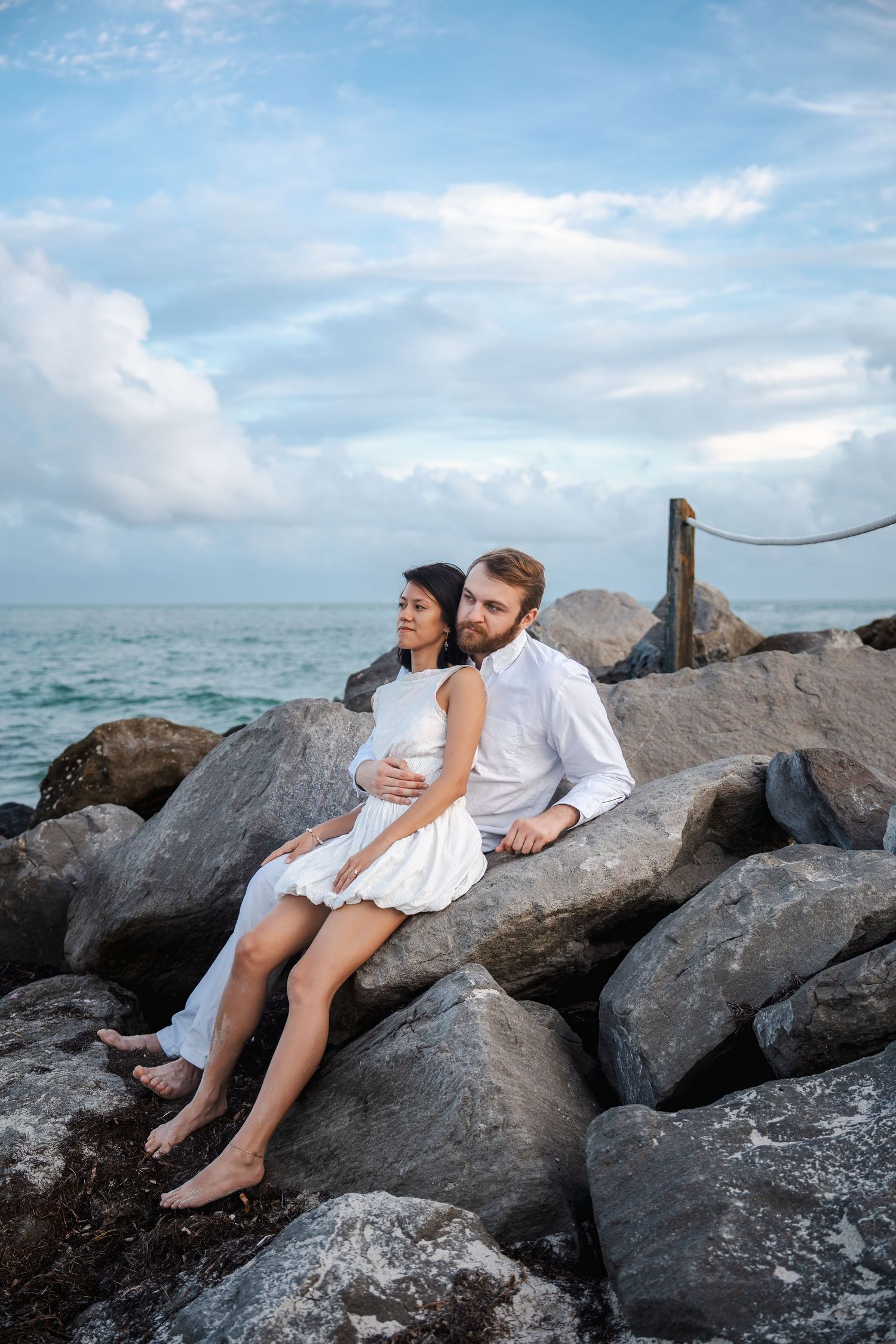 Engaged couple seated on coastal rocks during a romantic Bill Baggs engagement photo session.