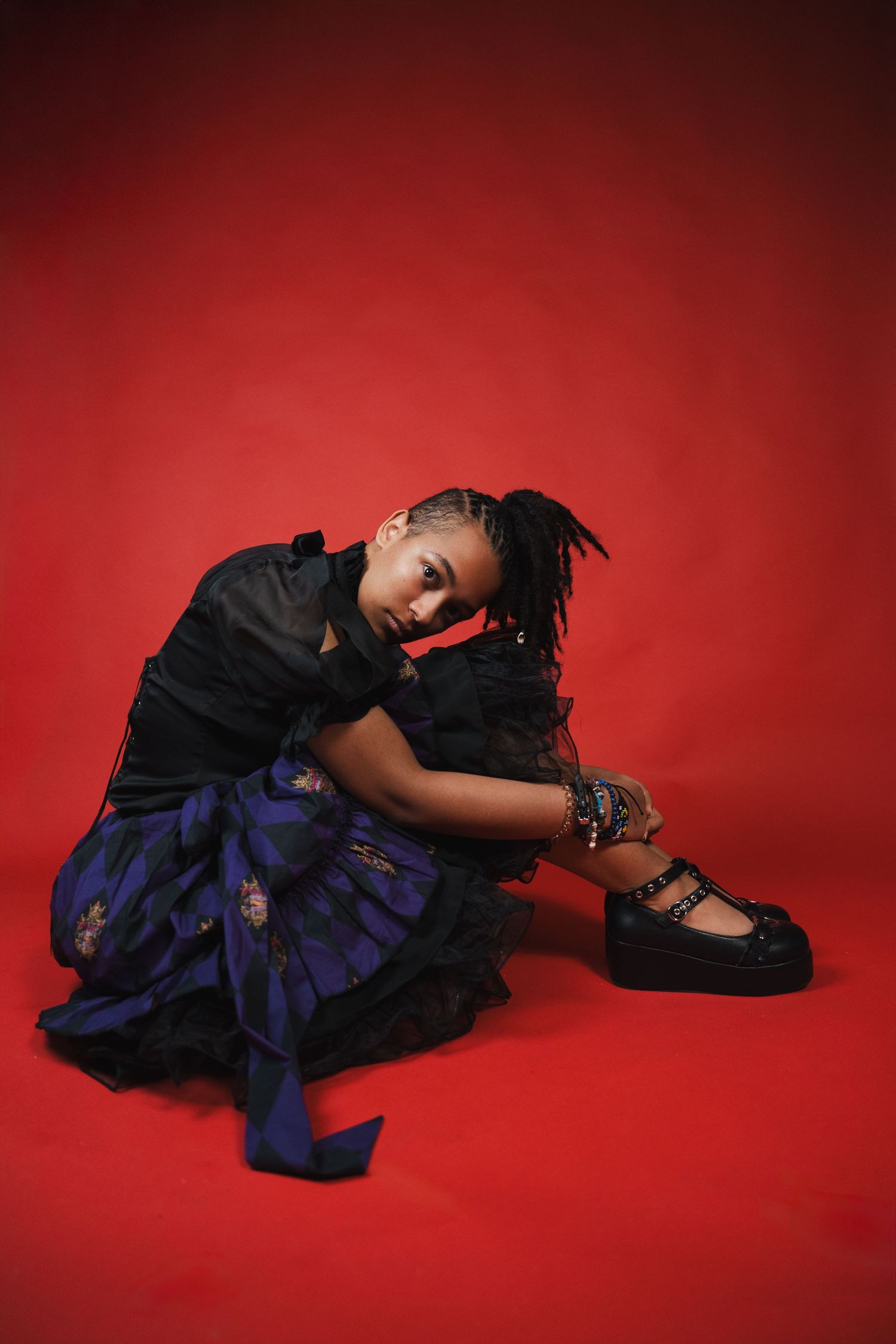 Creative studio senior portrait seated against a red backdrop with dramatic lighting and fashion-forward styling.