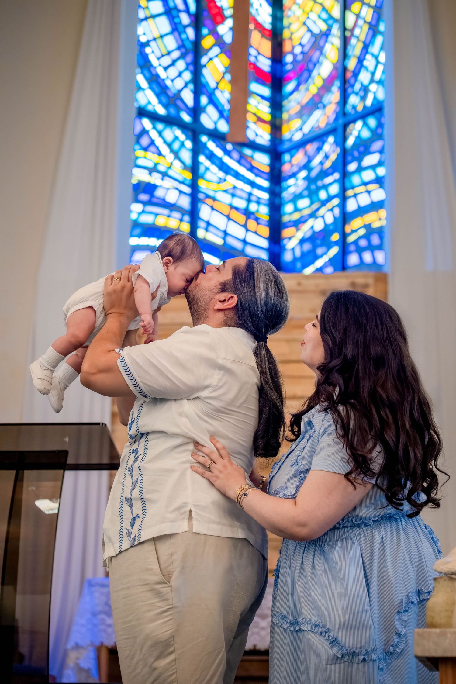 Family embracing while holding their baby during a baptism ceremony inside a church.