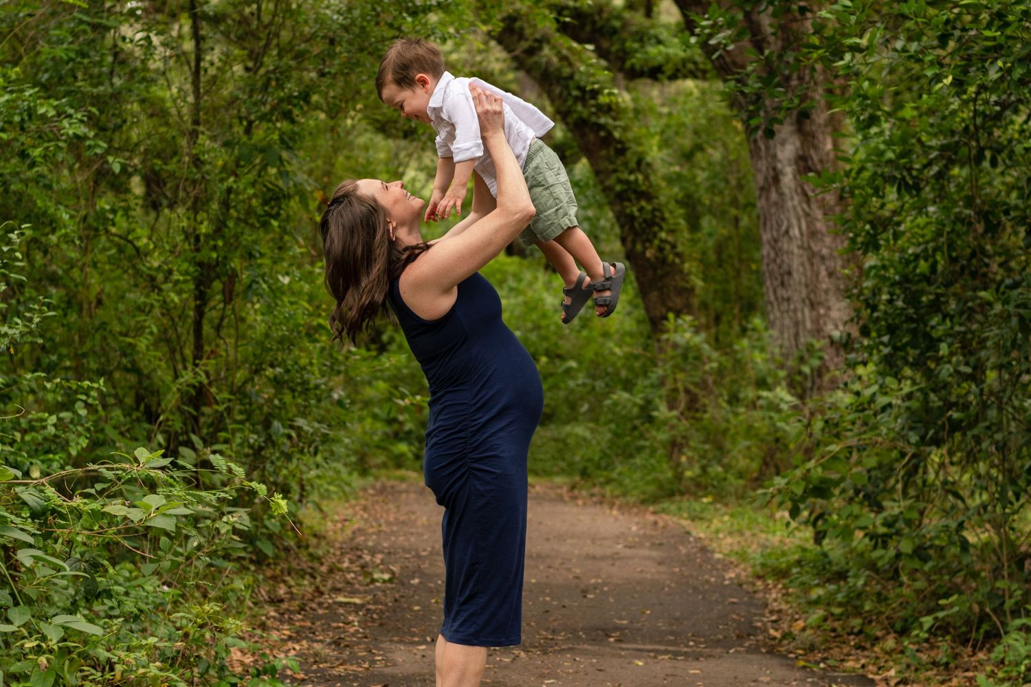 Maternity session at Tree Tops Park, Davie, FL – mother lifting her toddler in a lush green forest setting.