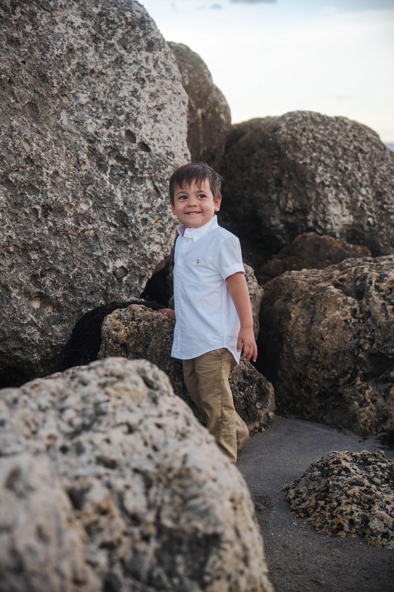 Young child standing between rocks during a beach pregnancy announcement session.