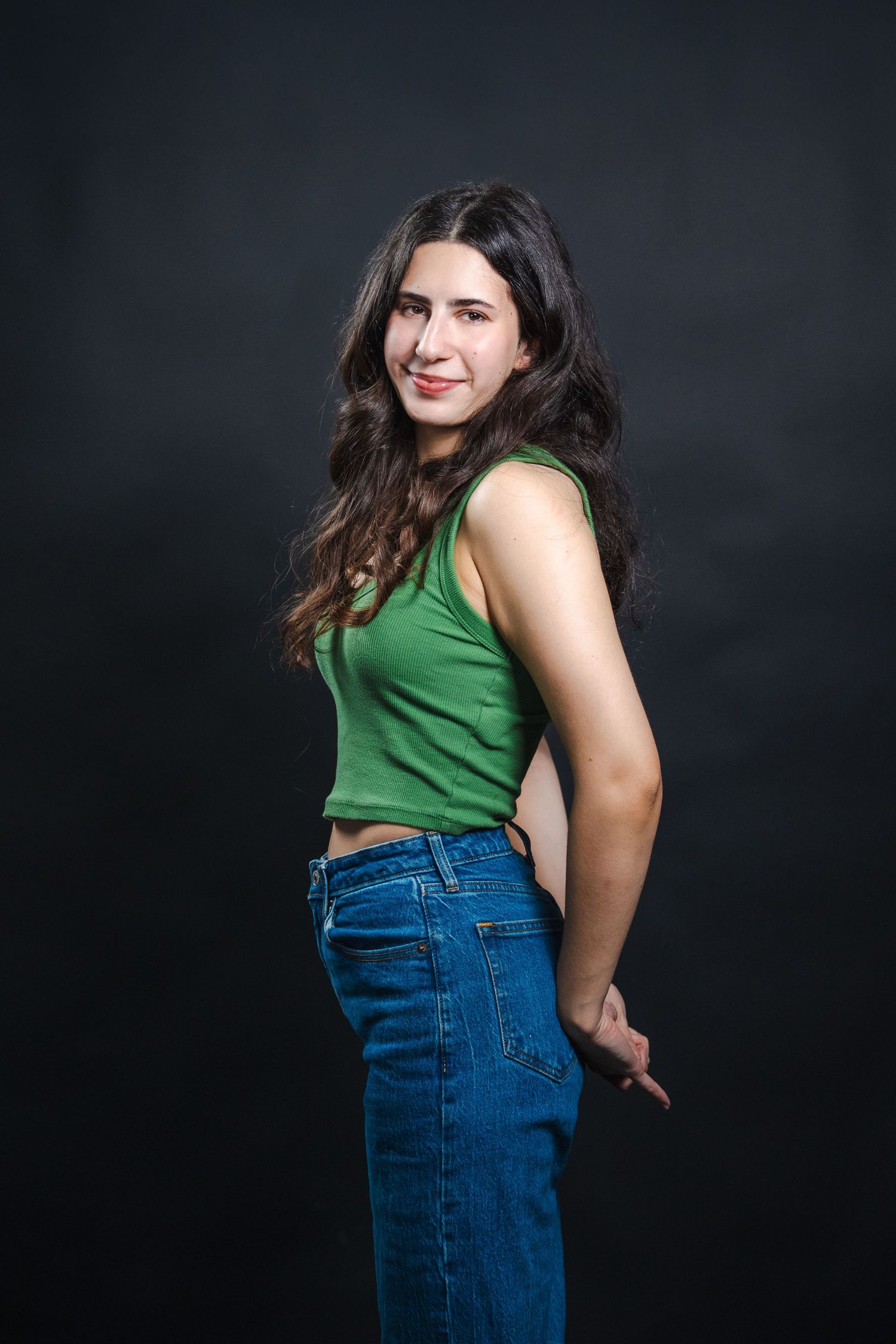 Full-length acting portrait of a woman posing confidently in a green top and jeans against a black studio backdrop