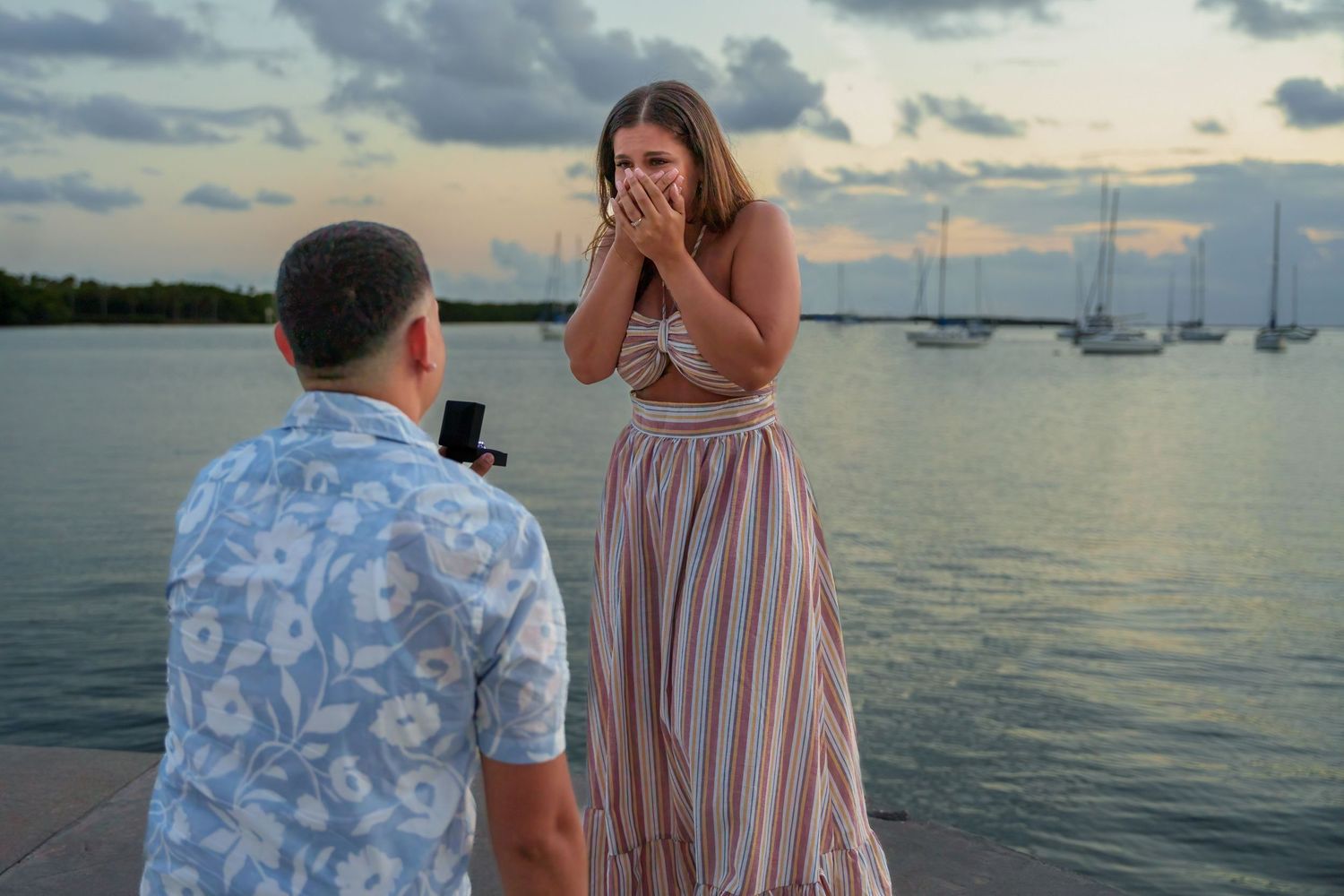 Emotional engagement session by the water, capturing a bride-to-be’s excitement during a heartfelt proposal at sunset.
