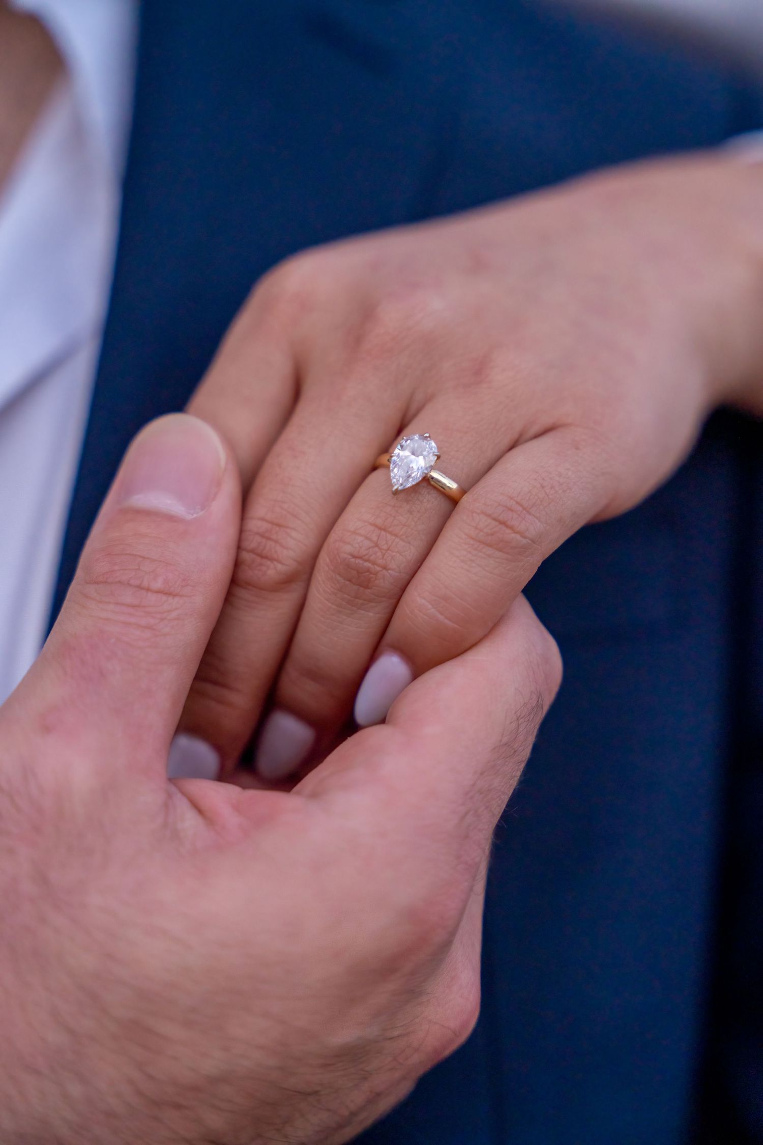 Detailed engagement ring shot, highlighting a sparkling diamond against a tailored navy suit for a classic, timeless look.