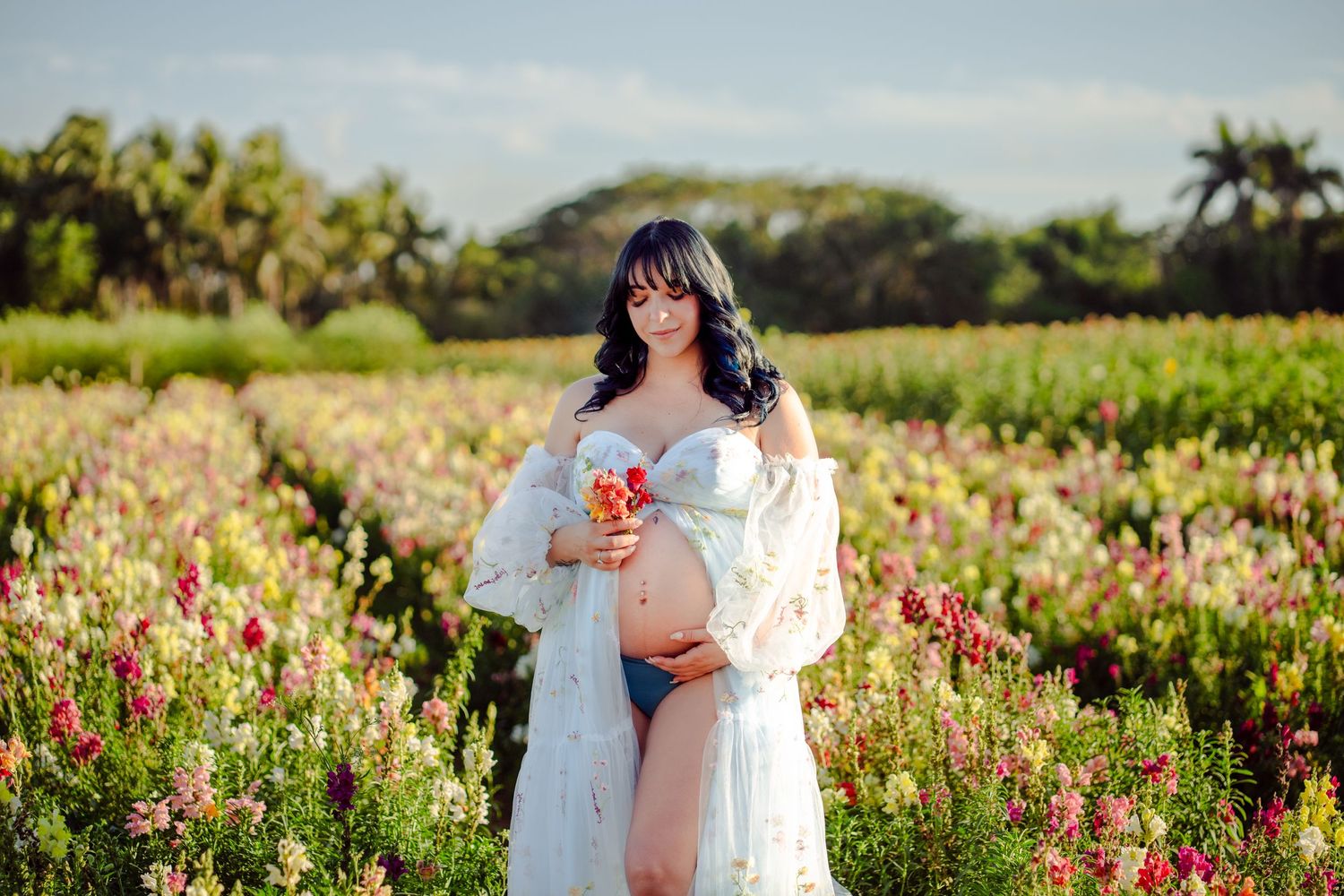 Full-body maternity portrait holding flowers, shot in a wildflower field in Miami.