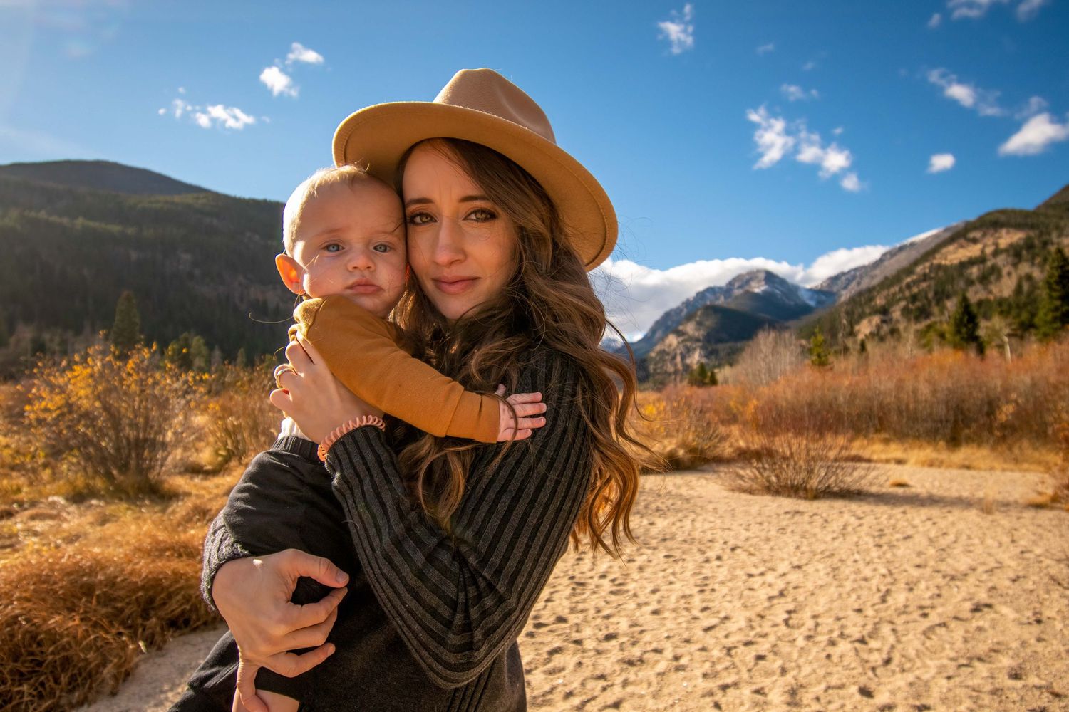 Emotive mother and baby portrait in Rocky Mountain National Park, CO – warm embrace with dramatic peaks behind them.