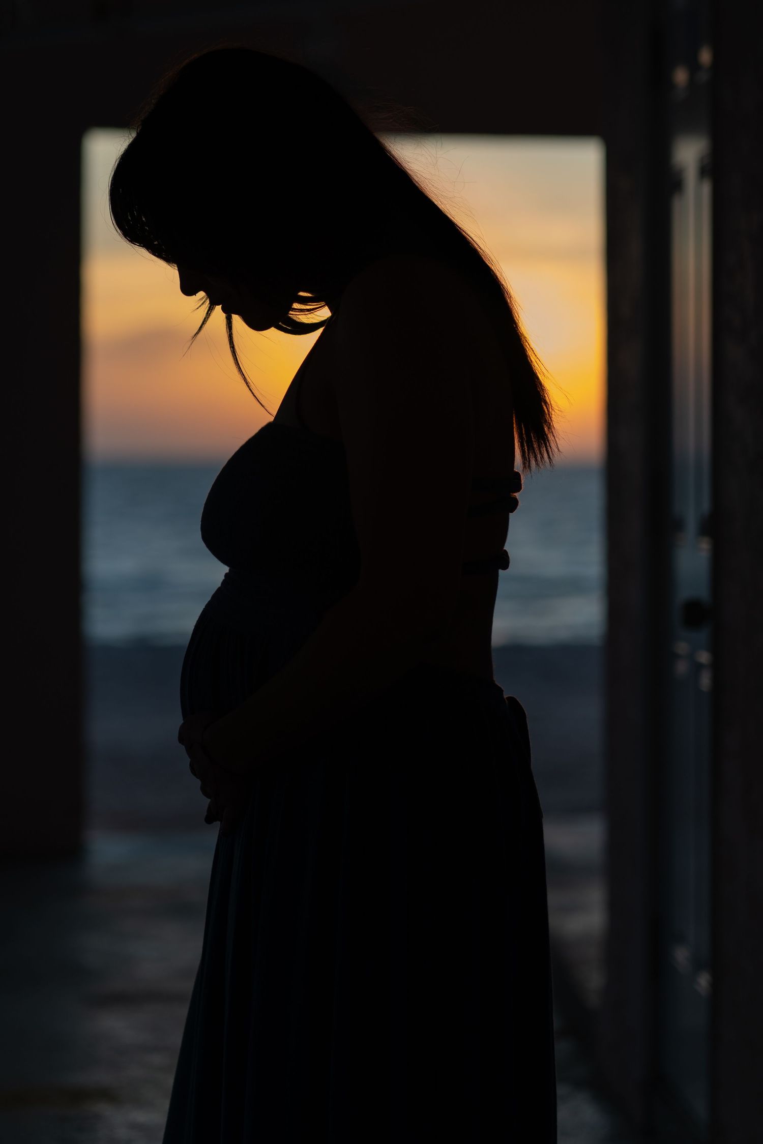 Dramatic maternity silhouette at Bonita Beach, capturing a peaceful moment with the ocean at sunset.