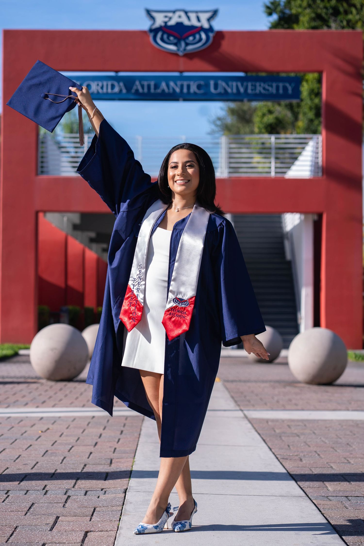 FAU graduation portrait of student raising cap in front of university archway in Boca Raton
