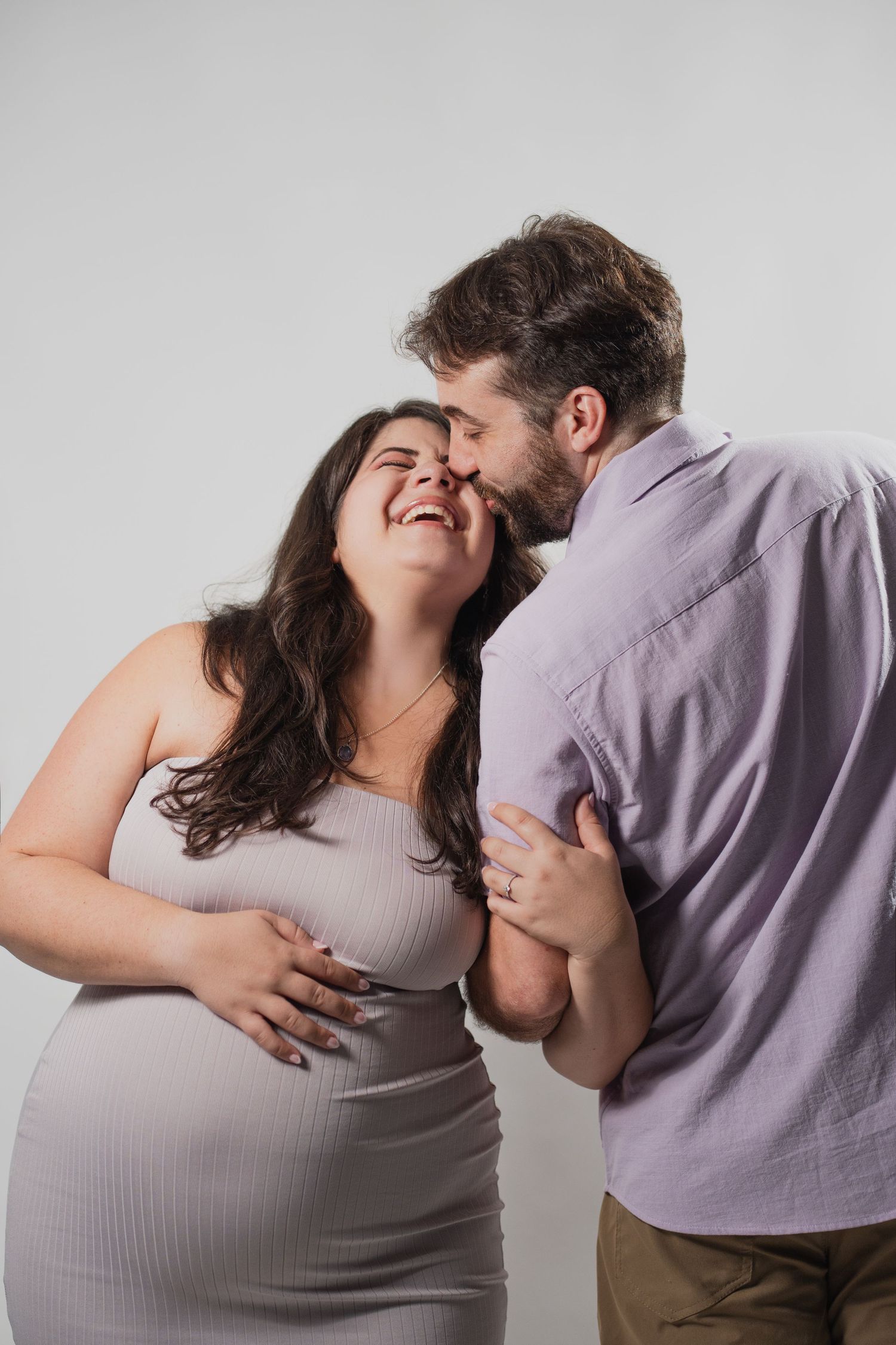Studio maternity photo of expectant mother smiling while partner kisses her cheek