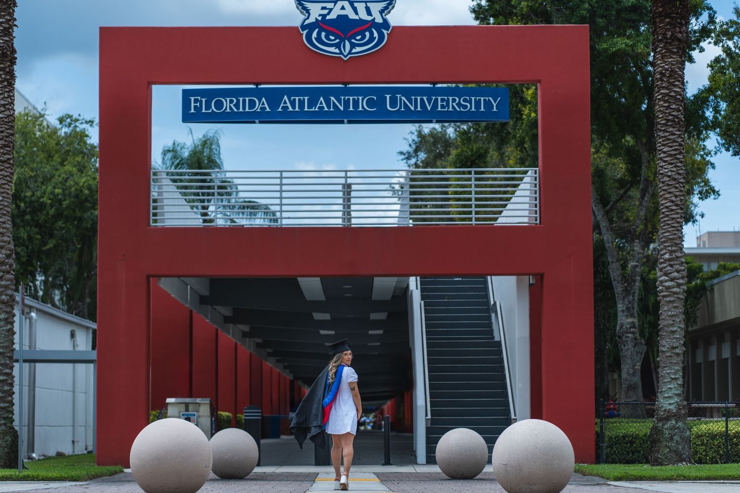 FAU graduate standing beneath the Florida Atlantic University sign, holding her gown over her shoulder, ready for her next journey.