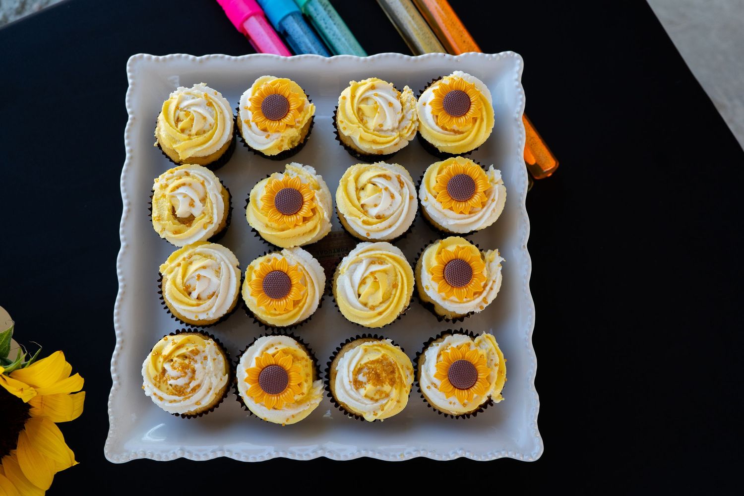 Overhead view of cupcakes arranged in a grid on a white plate, with vanilla cream and caramel toppings.