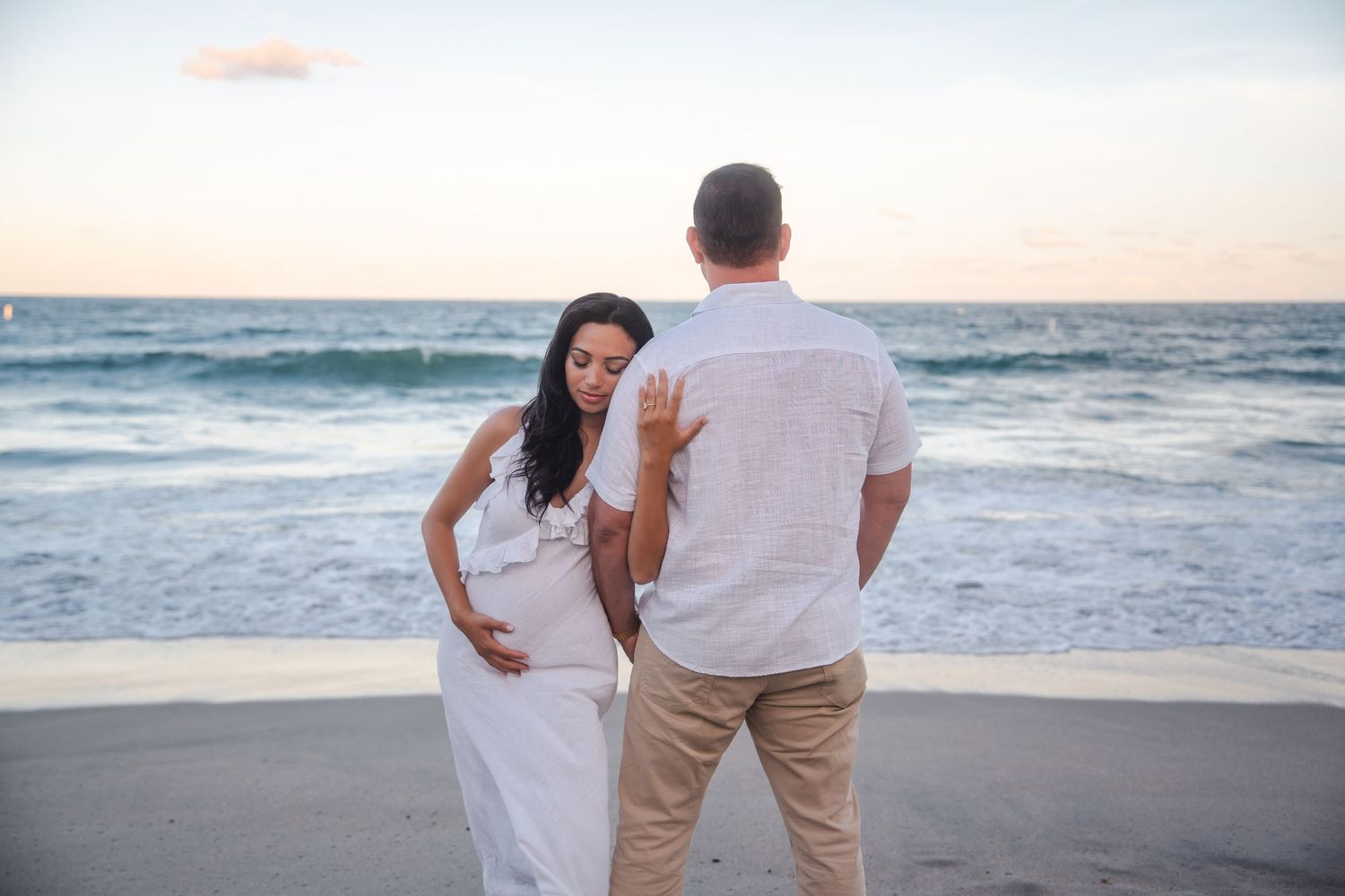 Candid pregnancy announcement portrait of an expecting couple walking along the shoreline, photographed at Deerfield Beach with a relaxed,