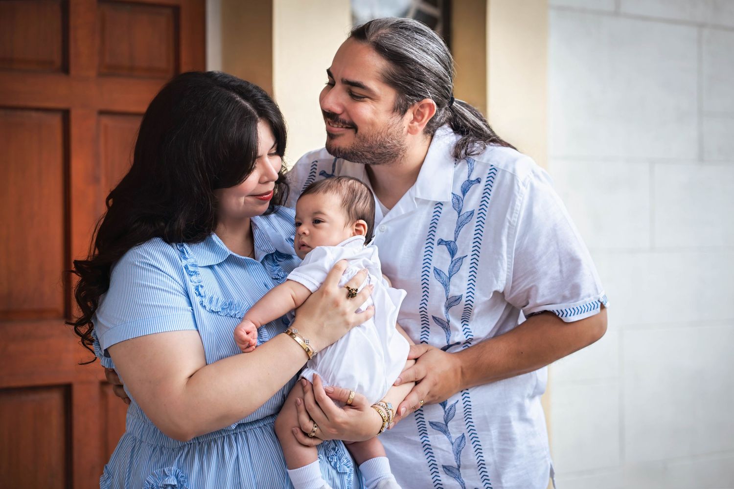 Parents holding their baby outside a church following a baptism ceremony, captured in natural light.
