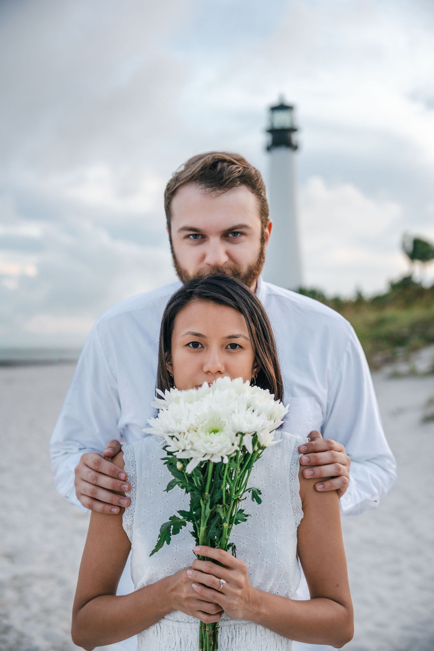 Engagement portrait of a couple holding flowers with the Bill Baggs lighthouse in the background.